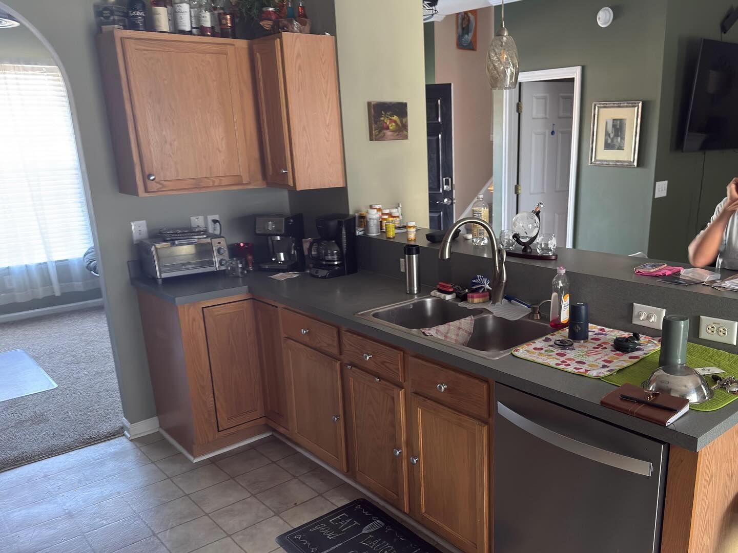 Kitchen with wooden cabinets, dark countertop, sink, and sunlight from a window.