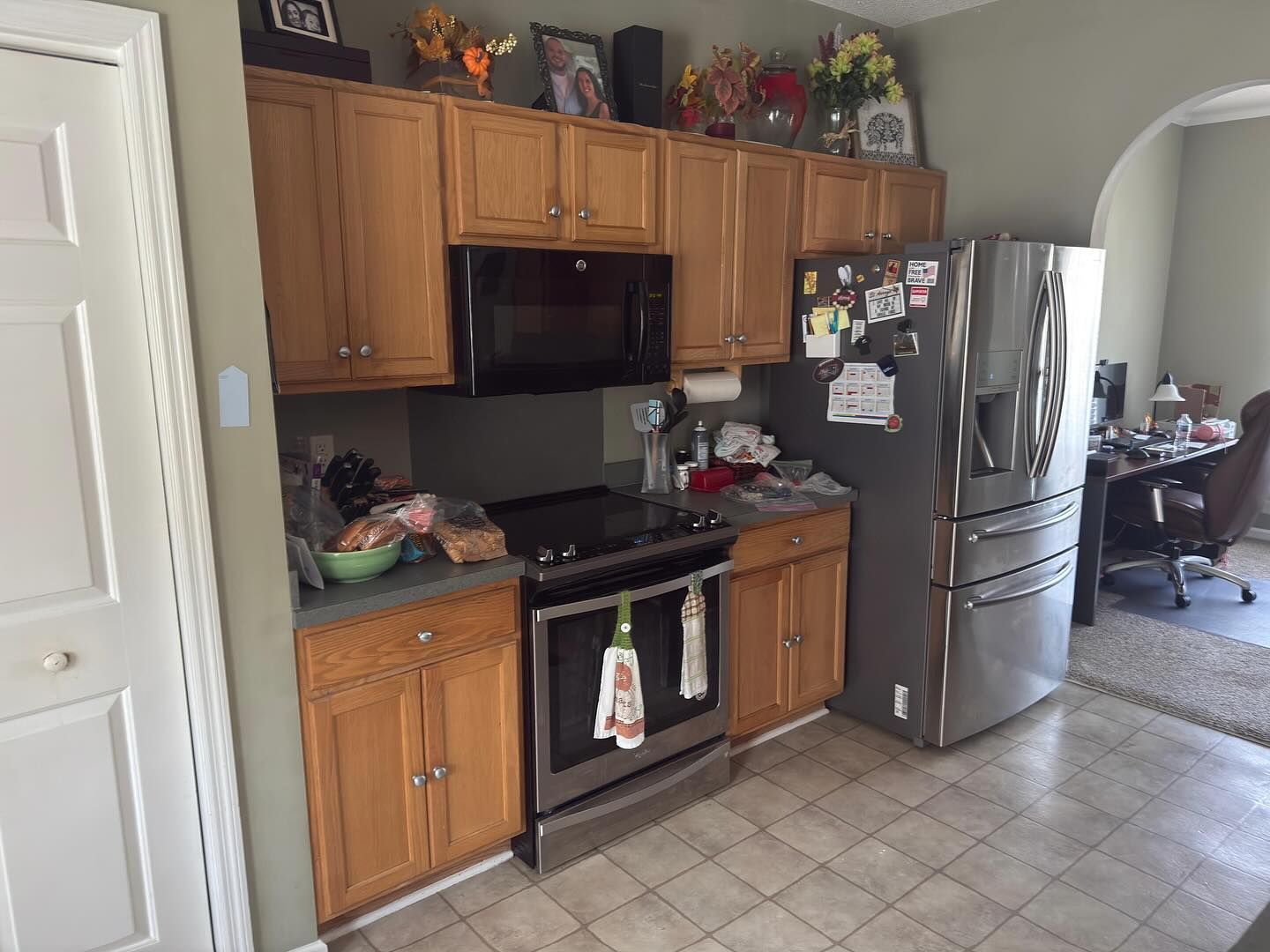 Kitchen with wood cabinets, stainless fridge, black stove, and tiled floor.