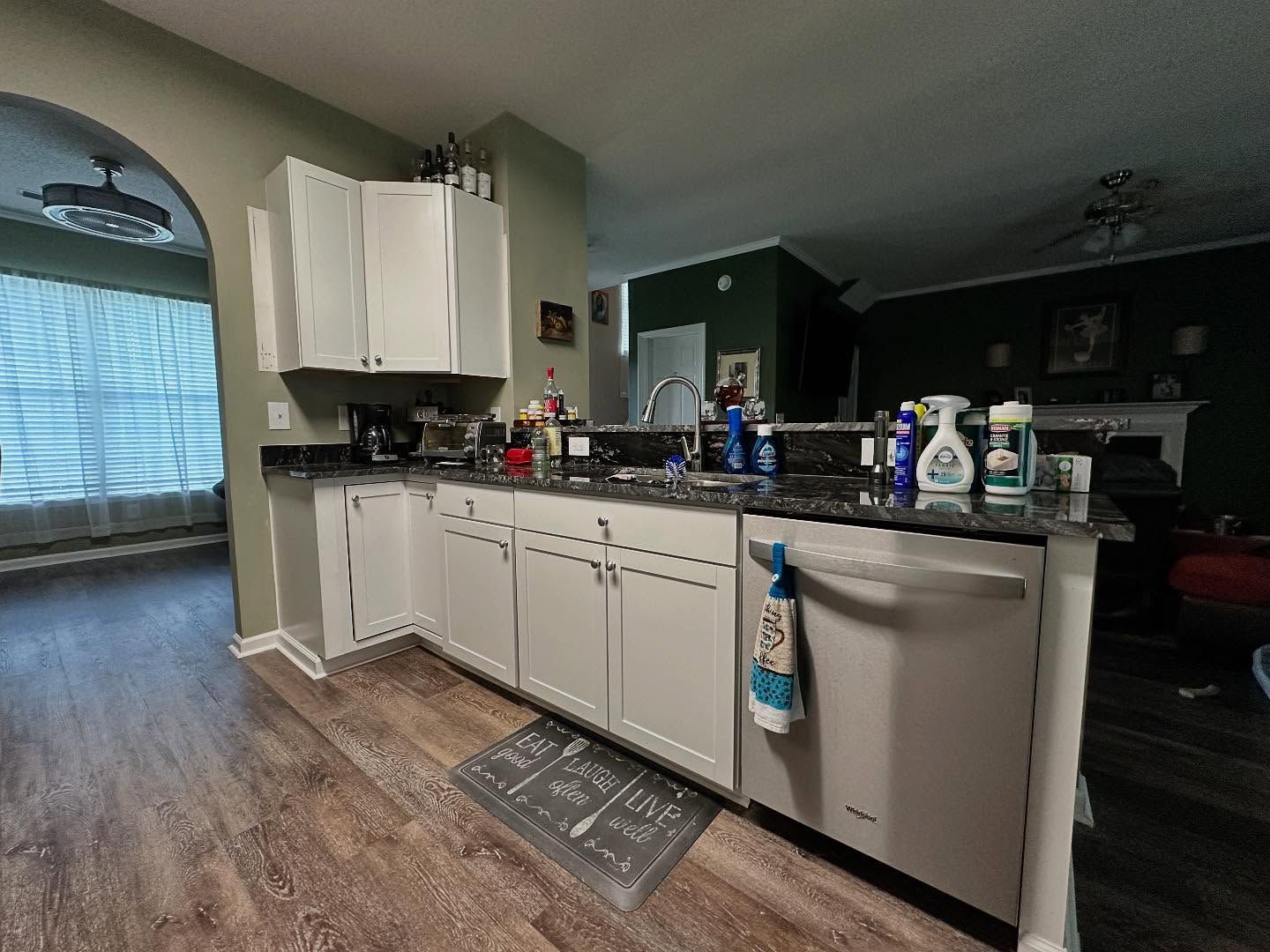 Modern kitchen with white cabinets, granite countertop, stainless dishwasher, and arched window into a living area