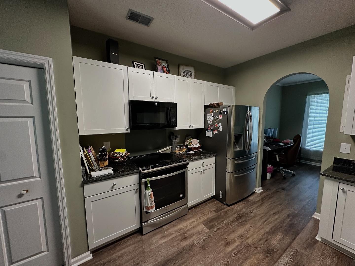 Kitchen with white cabinets, stainless-steel appliances, wood flooring, and an arched doorway to another room.