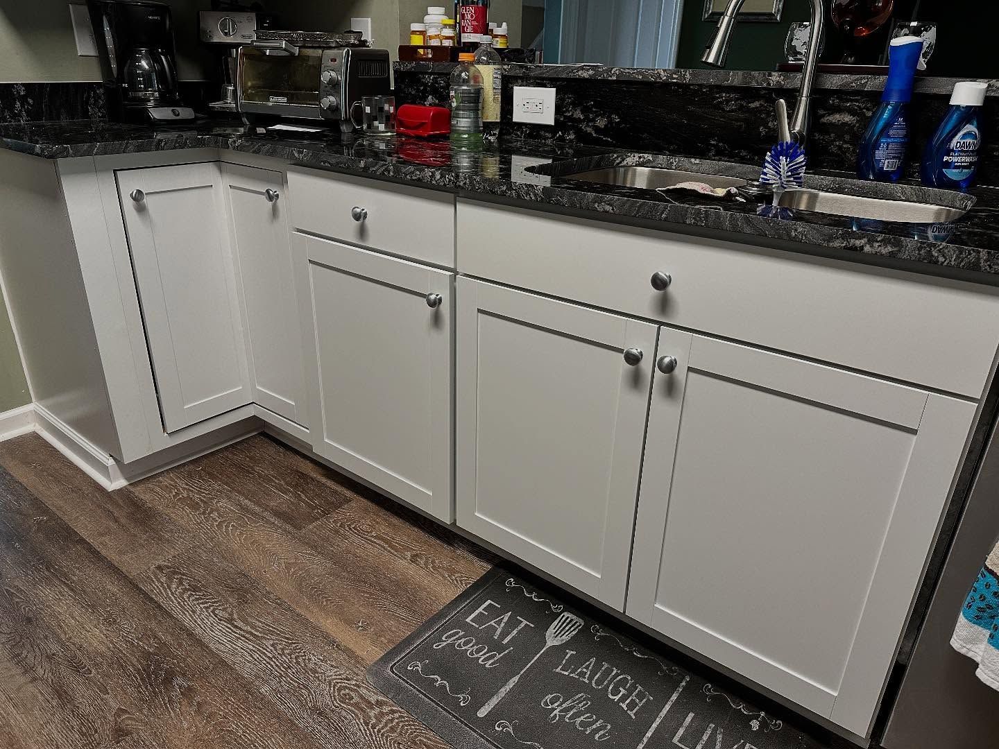 Kitchen lower cabinets under a granite countertop with a sink, plus a patterned floor mat on wood-look flooring