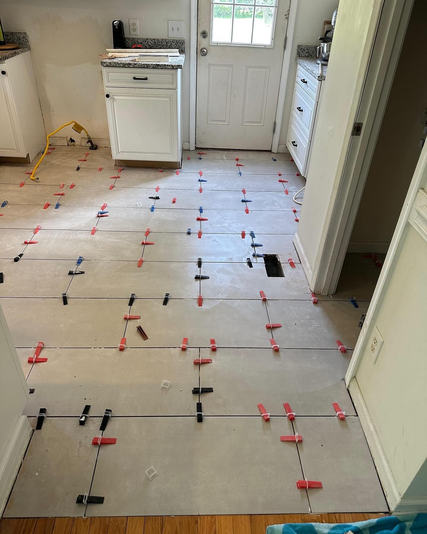 Kitchen floor under renovation with large gray tiles, spacers, and red leveling clips near a white door