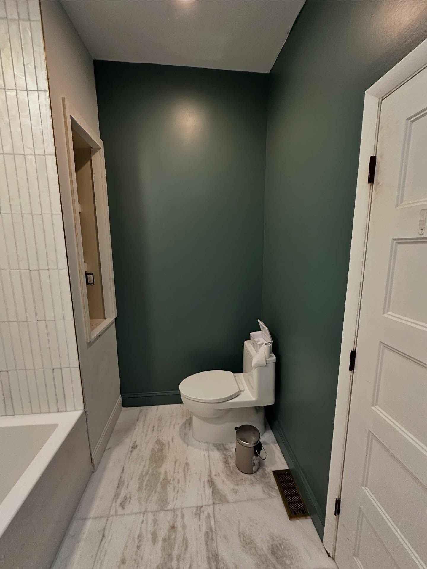 Small bathroom with green accent wall, white toilet, tiled floor, and door on the right.