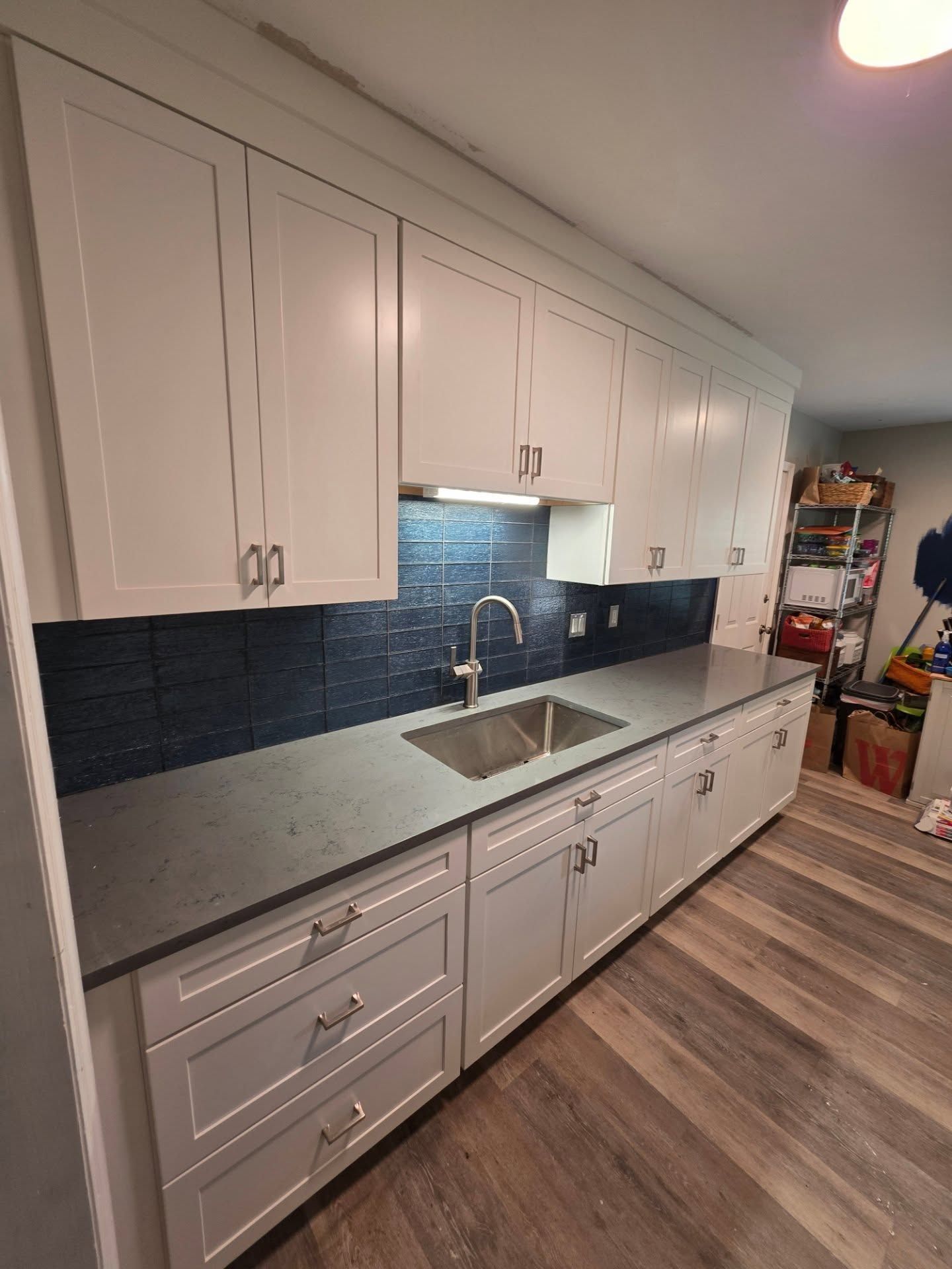 Modern kitchen with white cabinets, gray countertops, blue tile backsplash, and stainless sink on wood-look floor