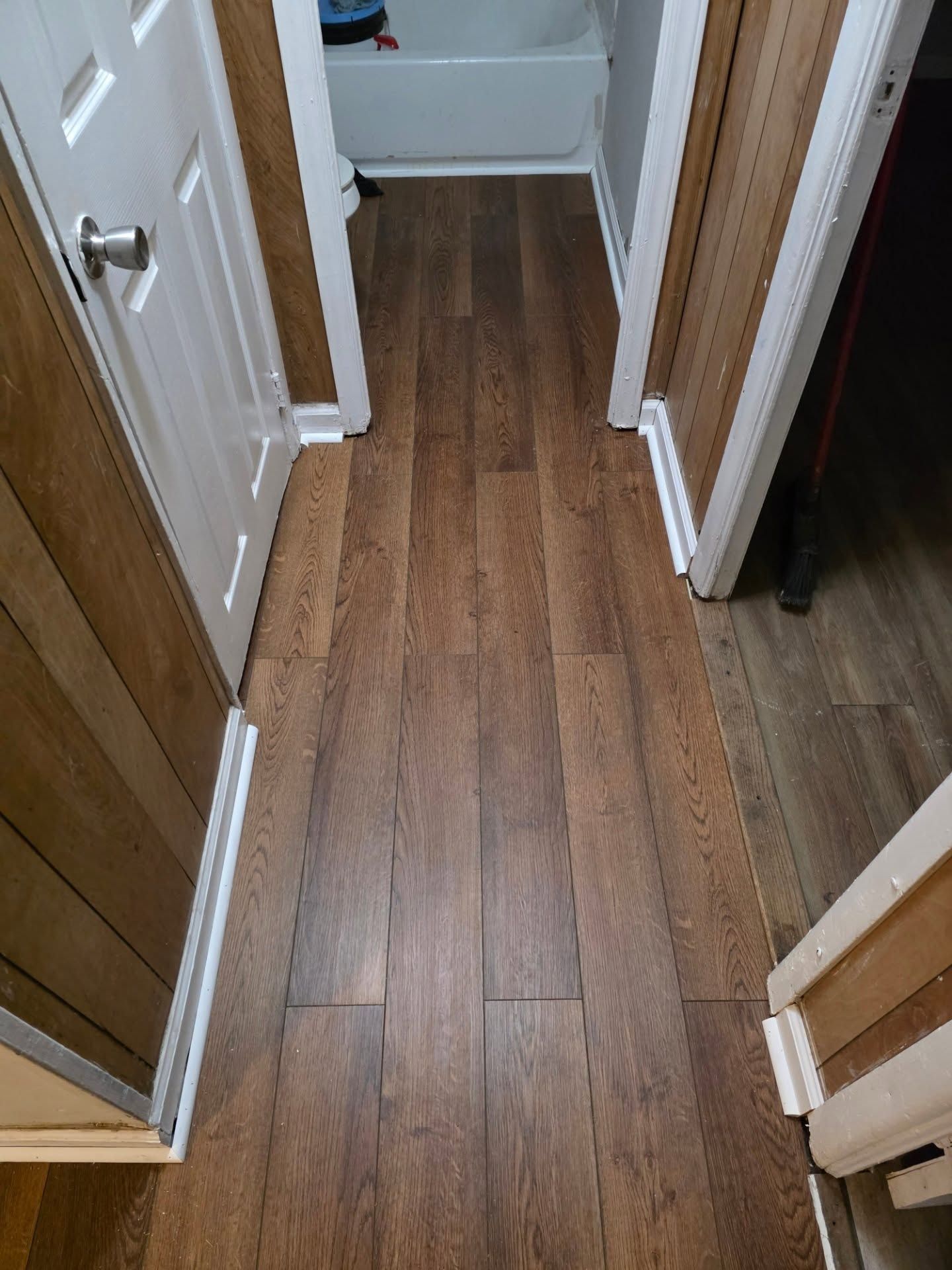 Narrow hallway with dark wood flooring, white doors, and mirrored closet panels.