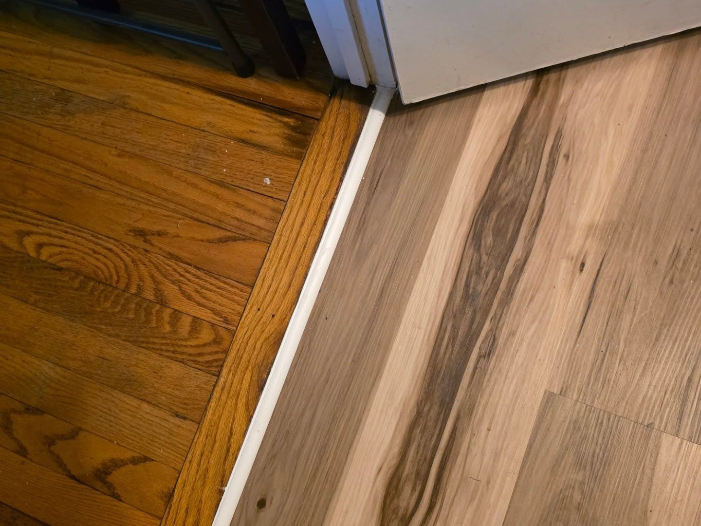 Wood and laminate flooring meeting at a doorway with a white transition strip