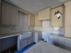 Small cream kitchen with cabinets, tiled backsplash, sink, stove, and countertop in a narrow room