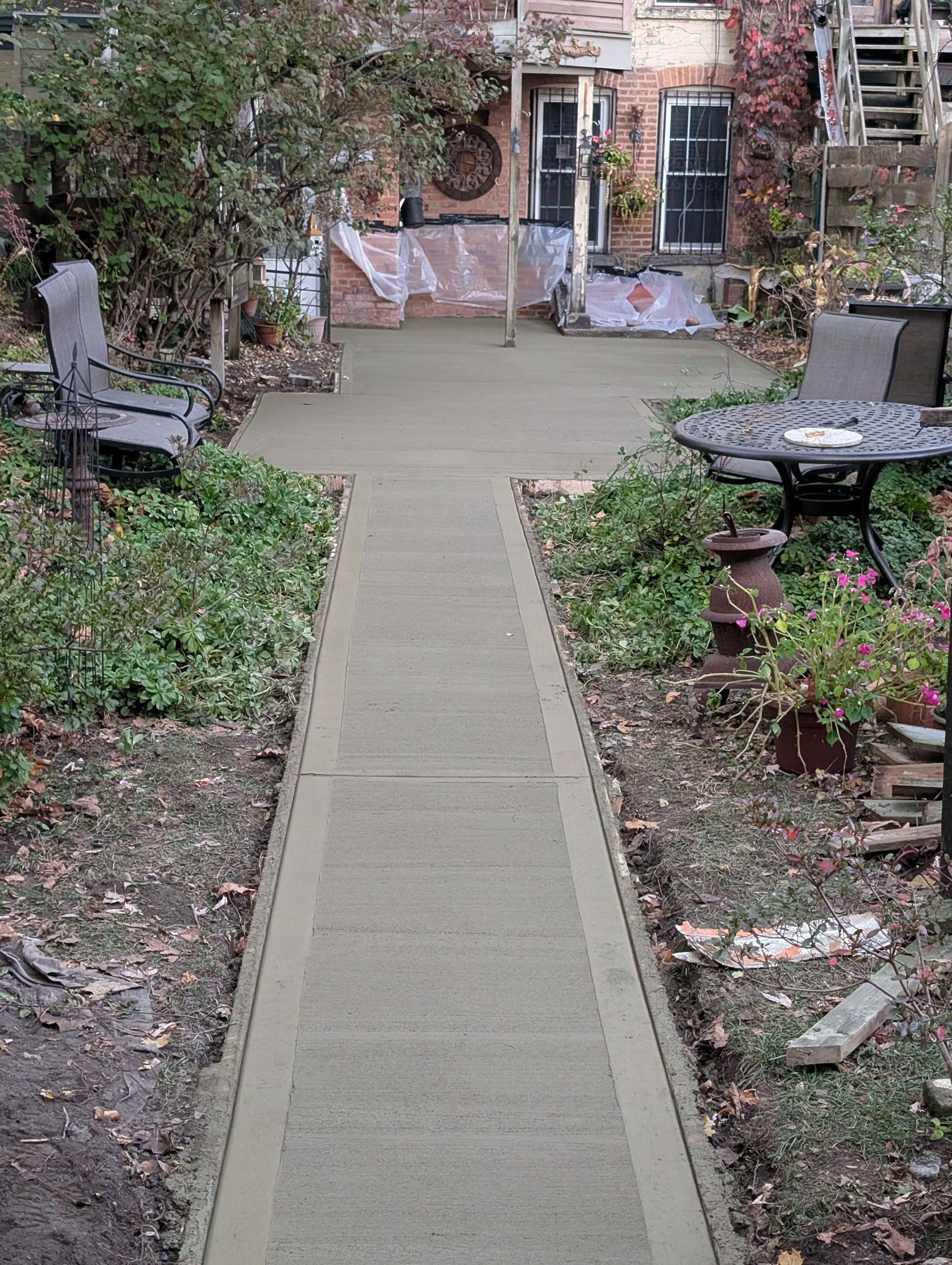 A concrete walkway leading to a house with a table and chairs.