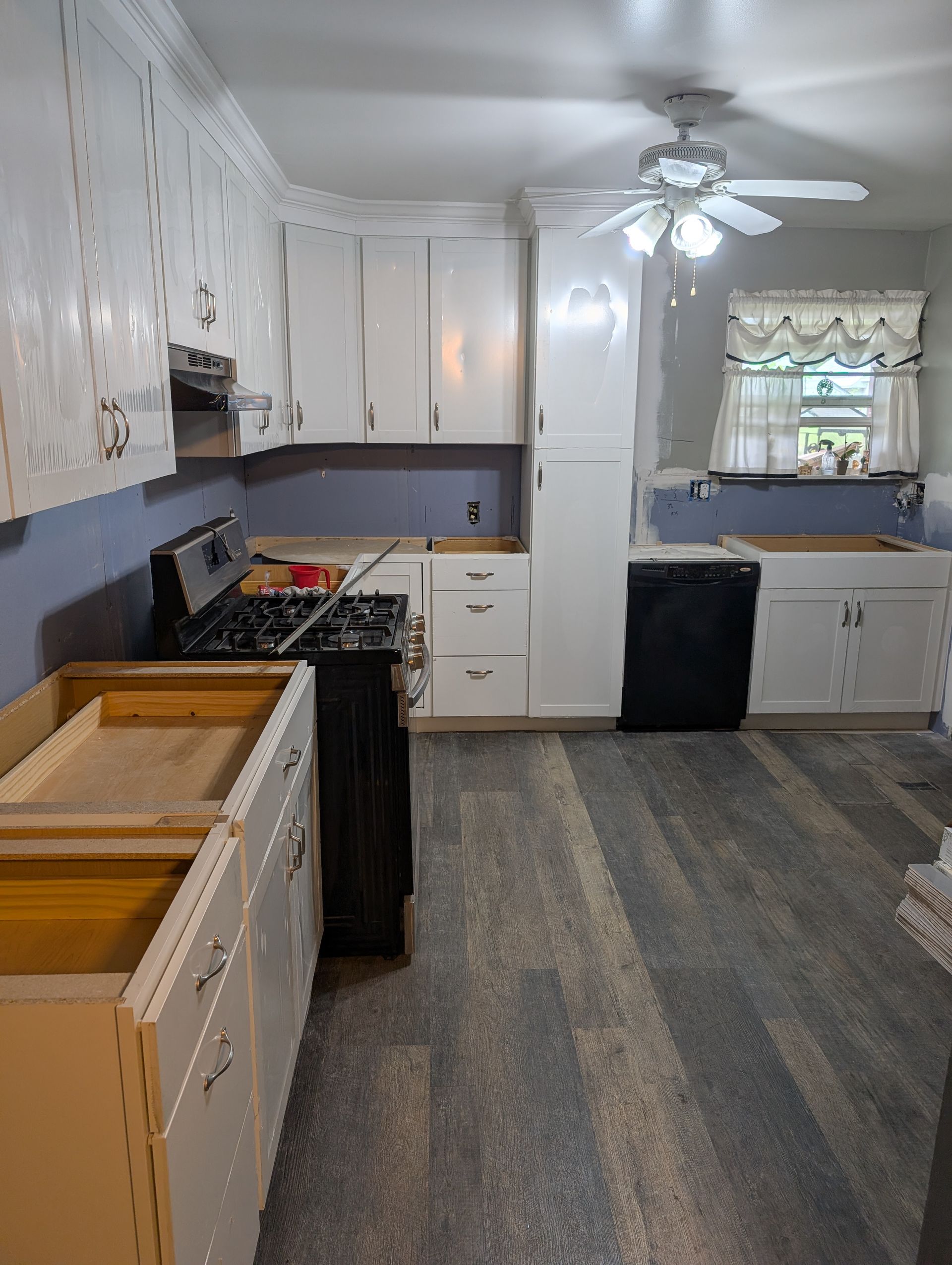 A kitchen with a stove , sink , cabinets and a ceiling fan.