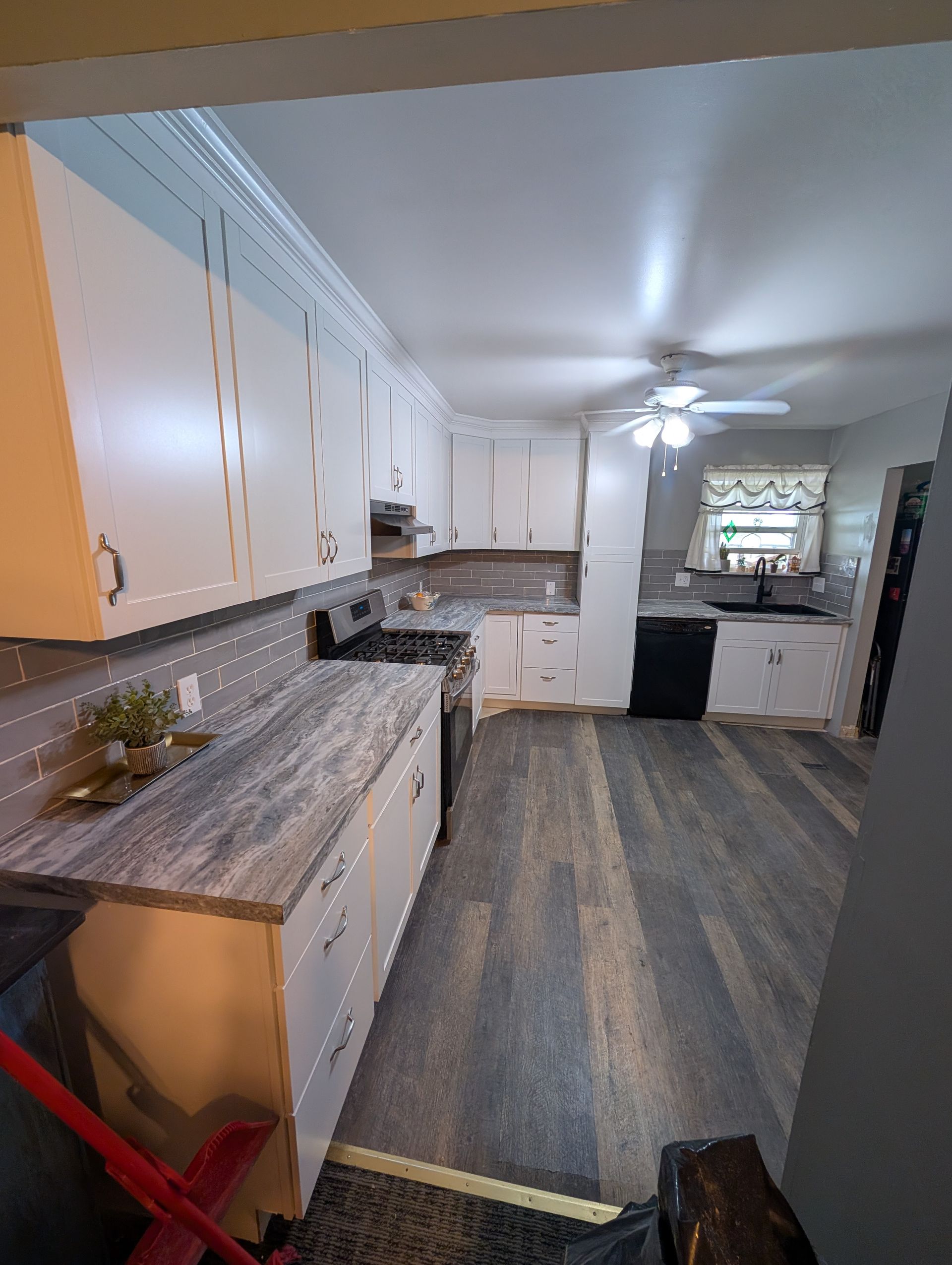 A kitchen with white cabinets , a stove , a sink , and a ceiling fan.