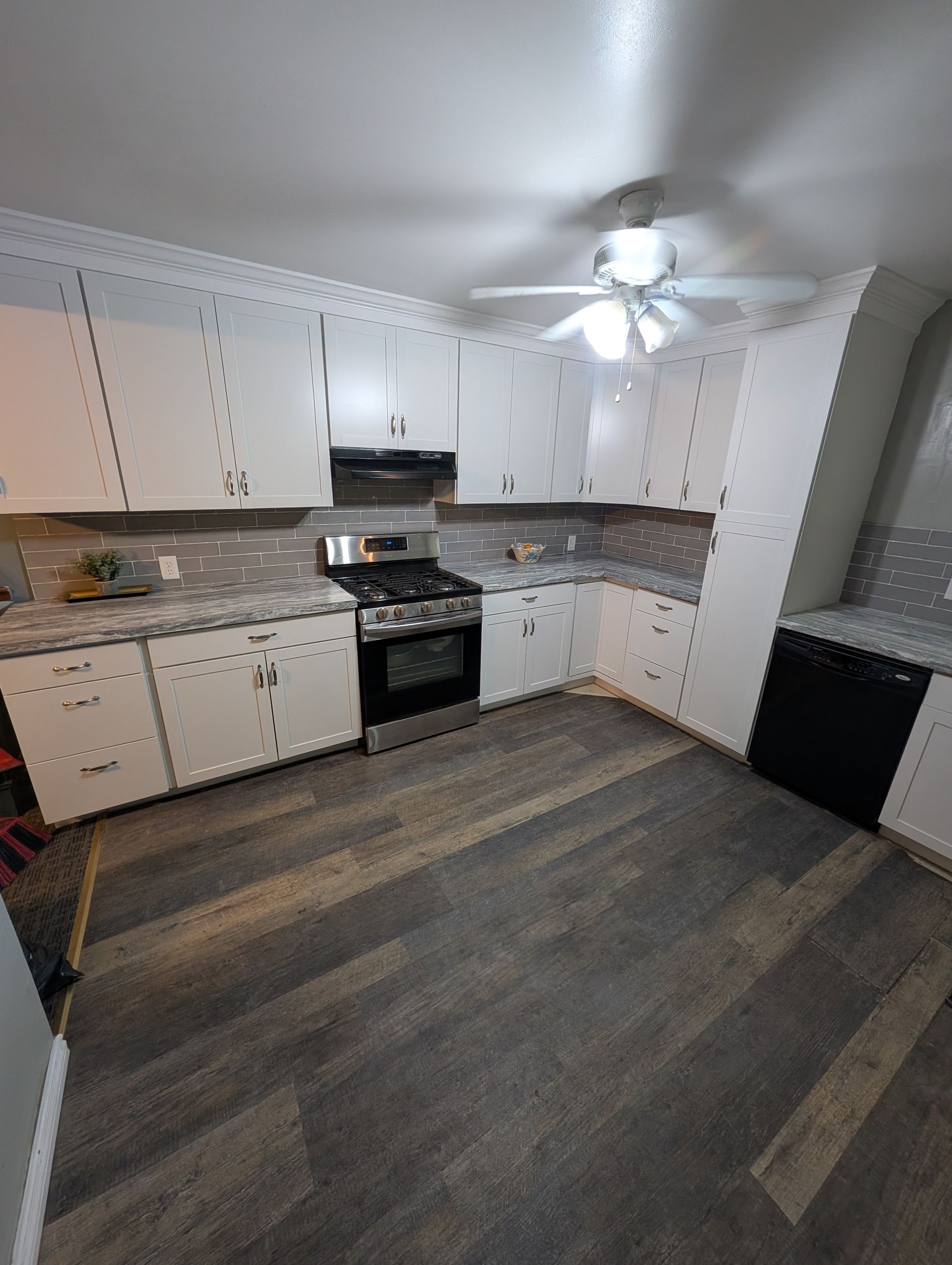 A kitchen with white cabinets , a stove , a dishwasher and a ceiling fan.