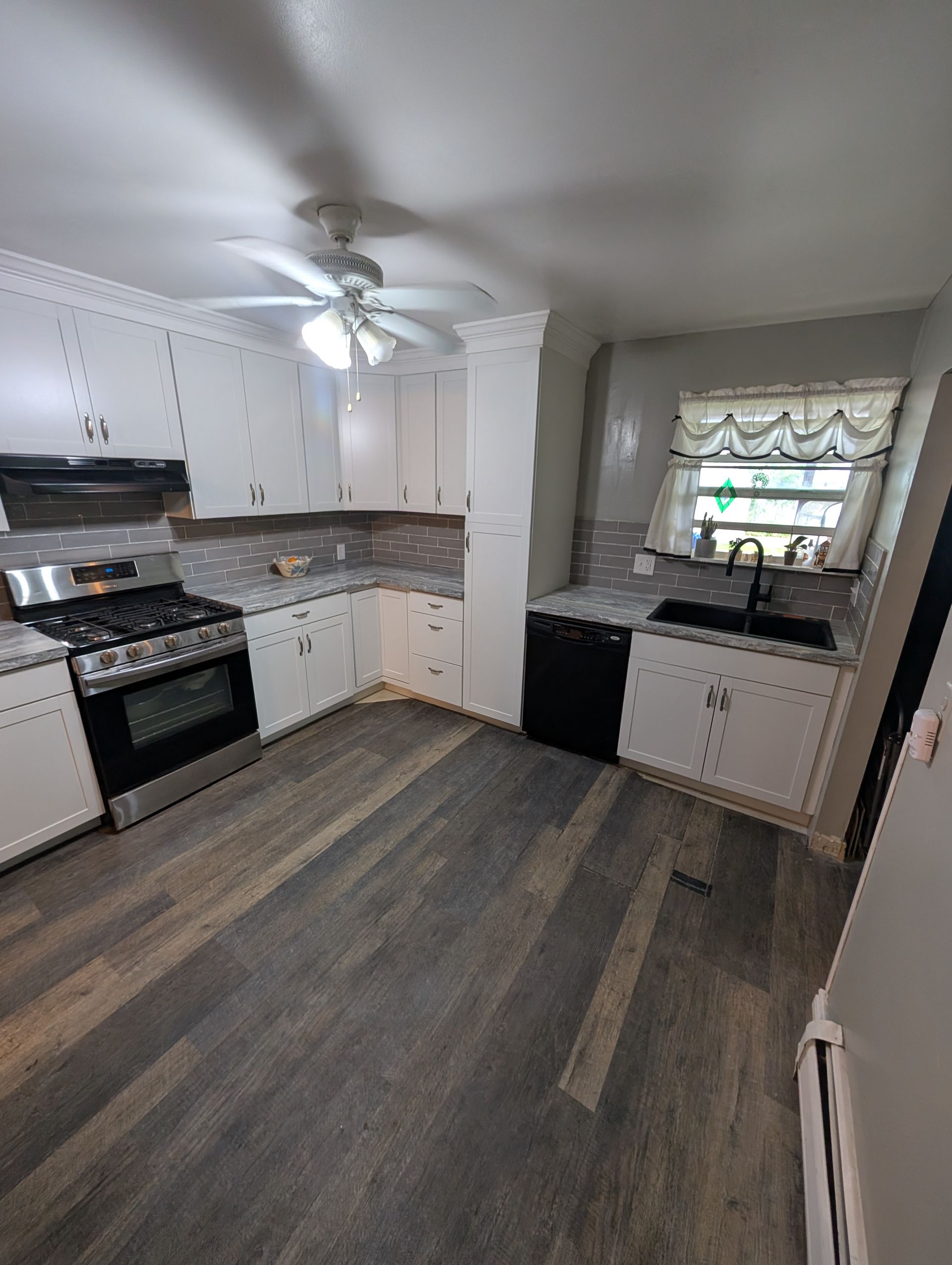 A kitchen with white cabinets , a stove , a sink , and a ceiling fan.