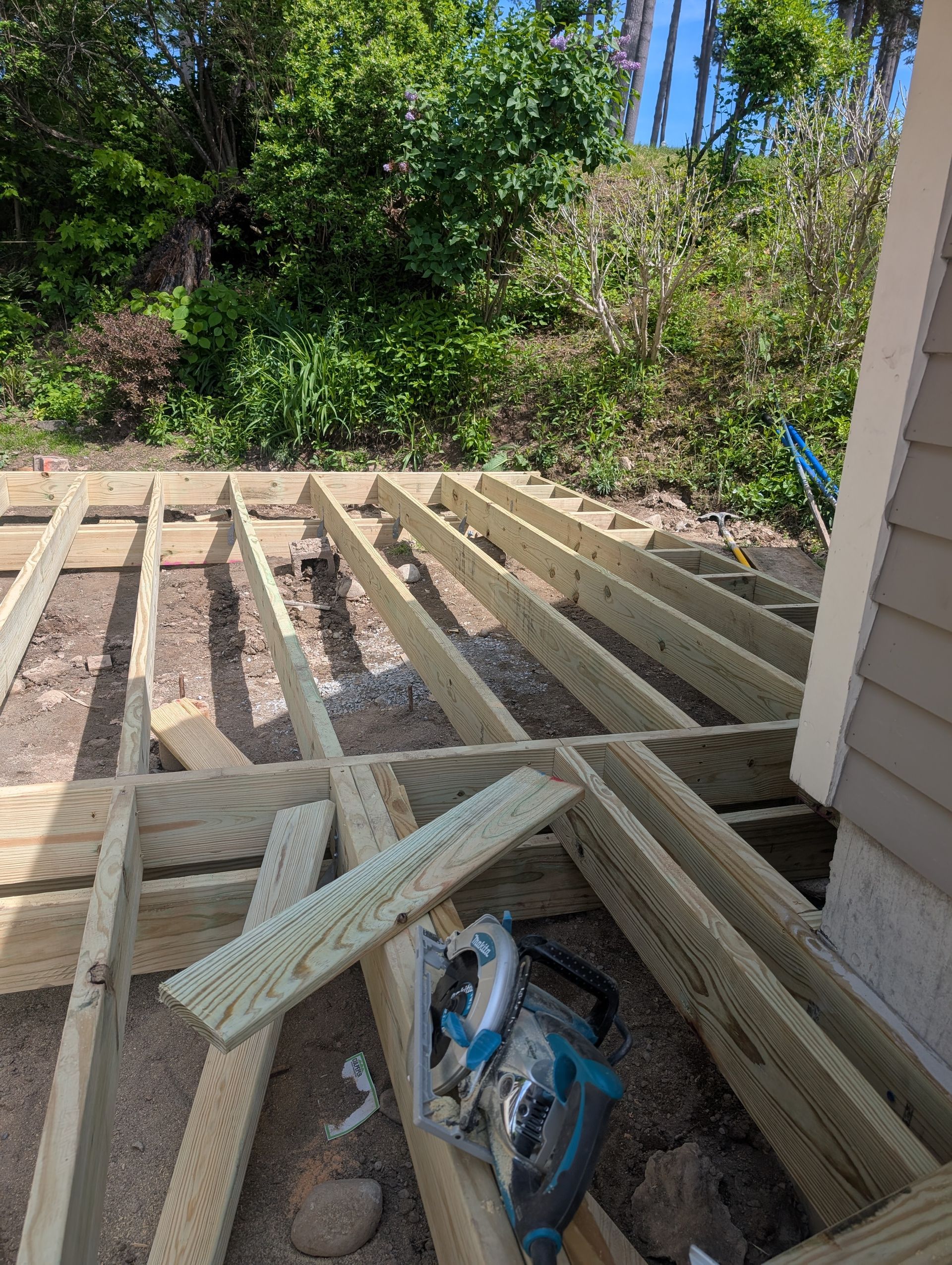 A circular saw is sitting on the ground next to a wooden deck under construction.