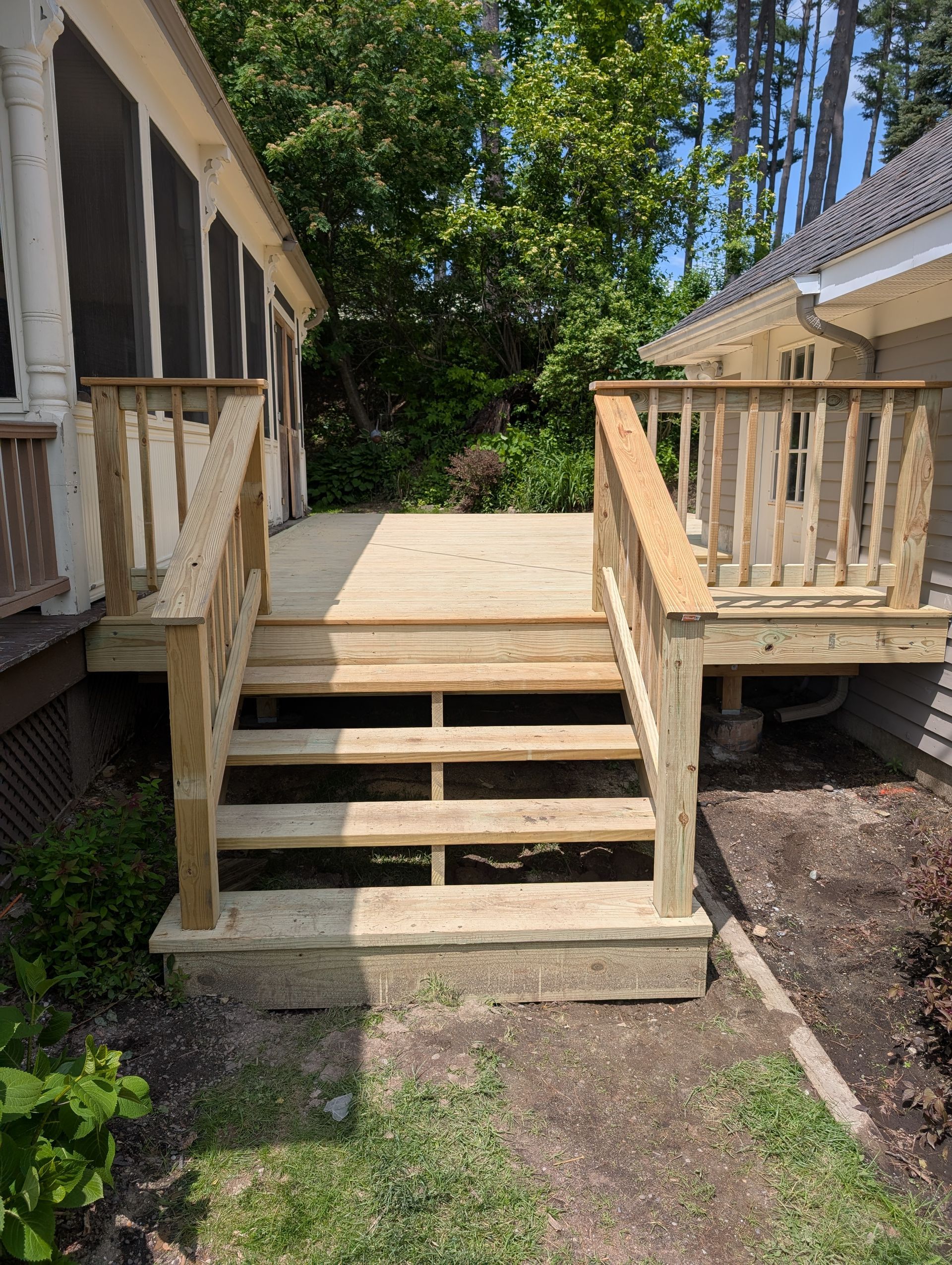 A wooden deck with stairs leading up to a screened in porch.