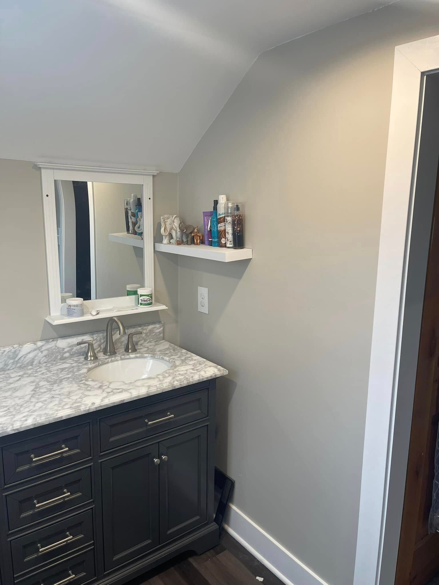 Small bathroom vanity with marble countertop, mirror, wall shelf, gray walls, and tiled floor.
