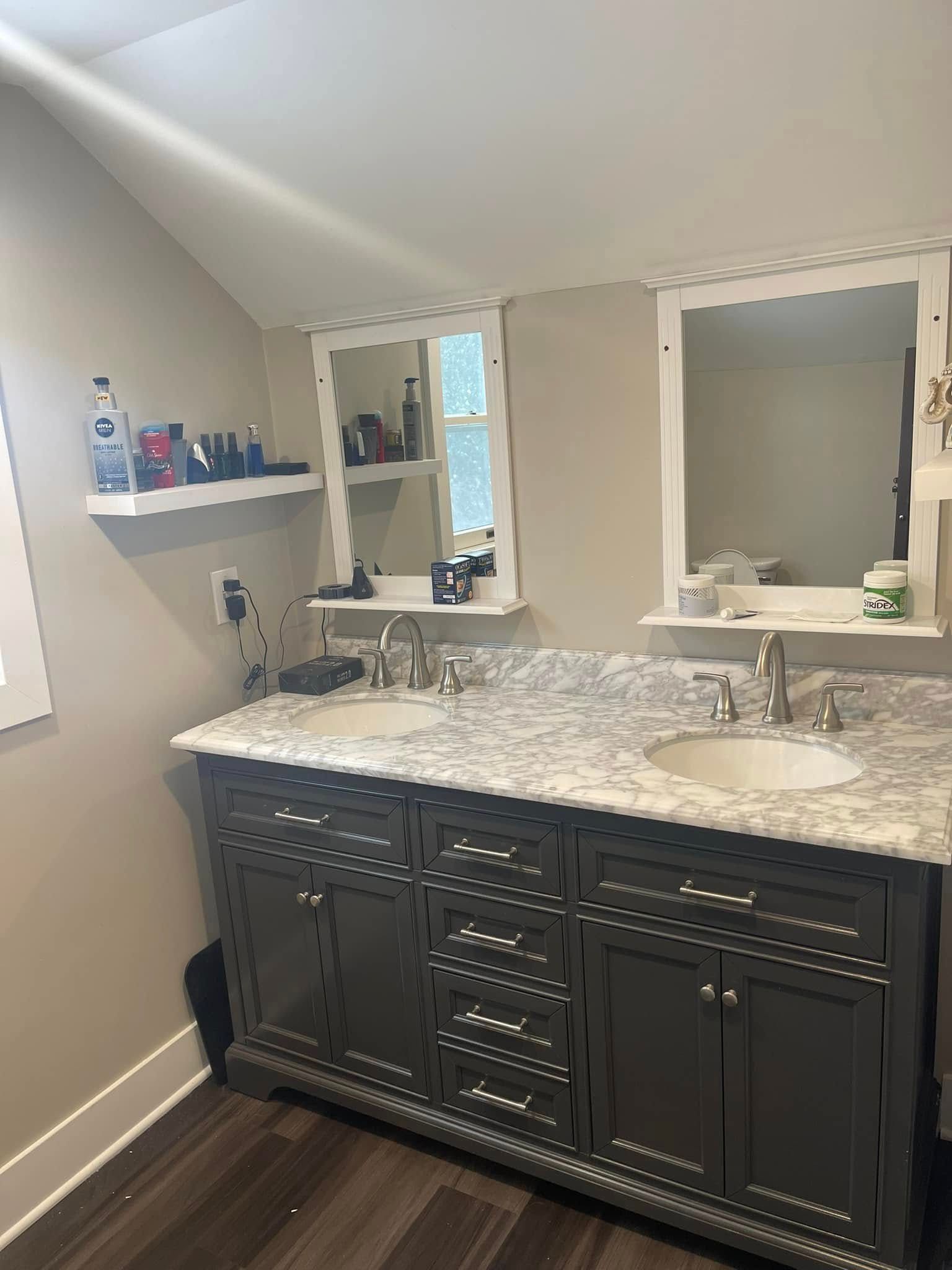 Bathroom vanity with granite countertop, double sinks, and large mirrors on a beige wall.