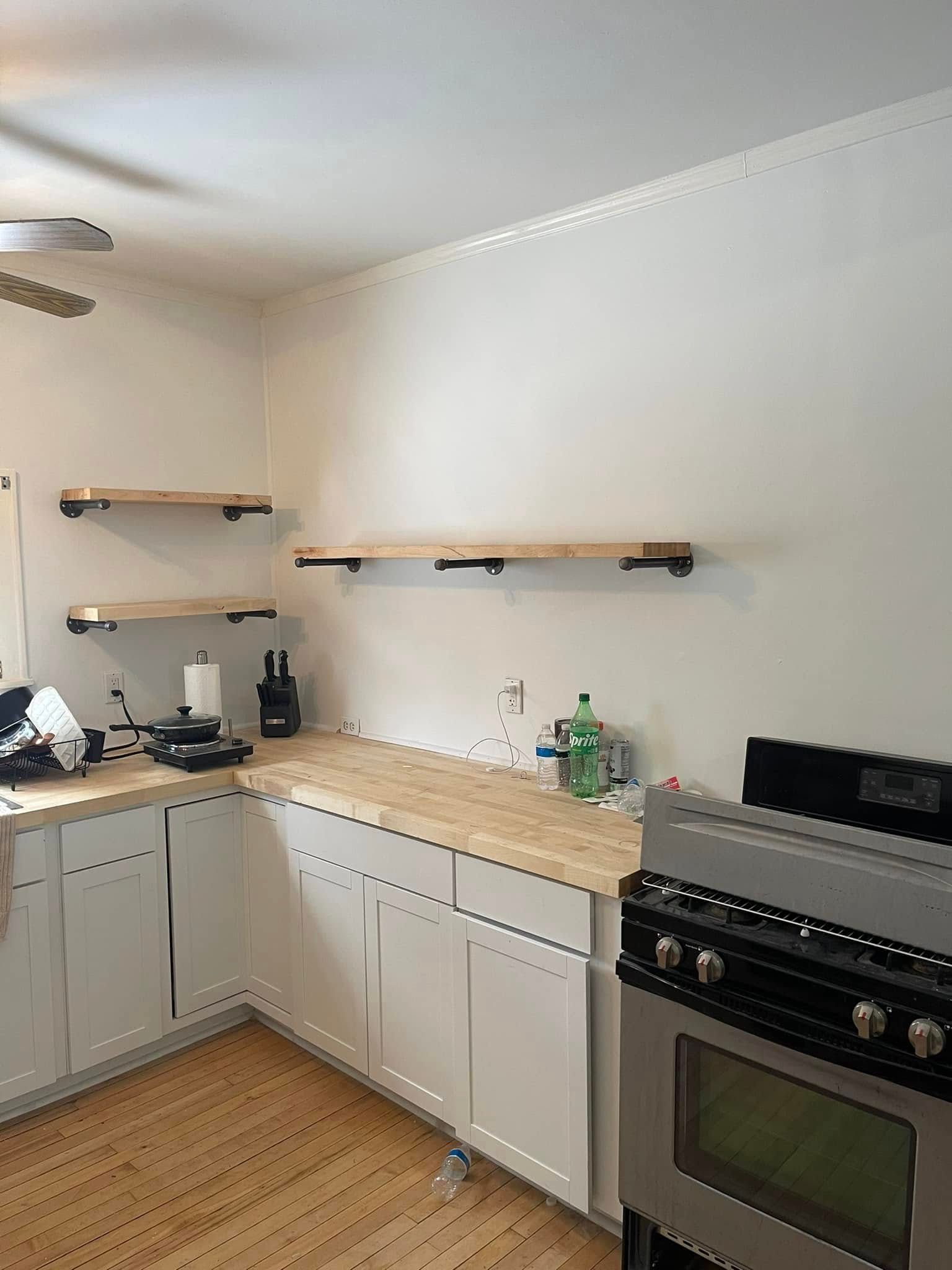 Bright kitchen with white cabinets, wood countertops, open shelves, and a stainless stove.