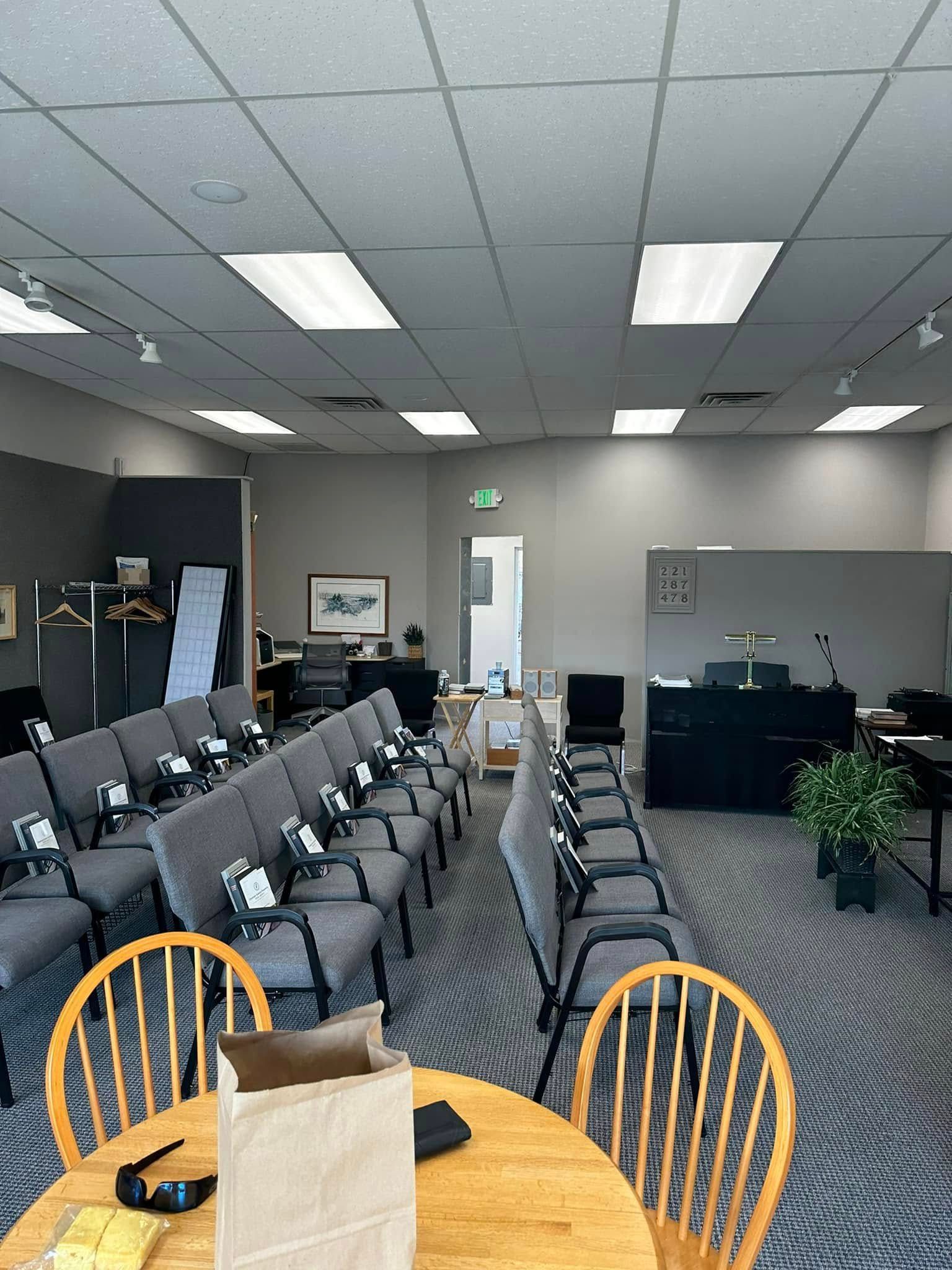 Empty conference room with rows of chairs, a round table, and overhead fluorescent lights