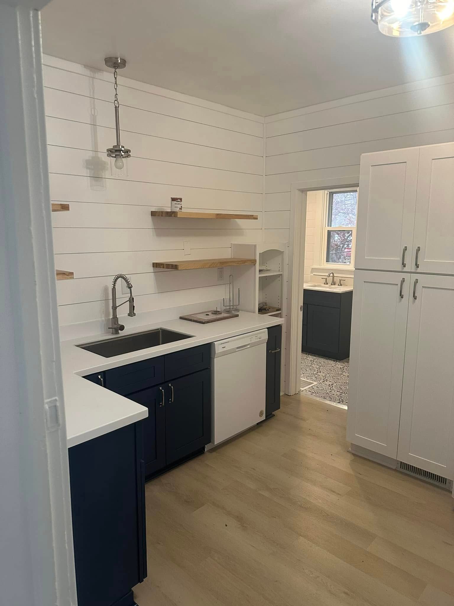 Small white kitchen with black sink, open shelves, white fridge, and light wood floor near a doorway.