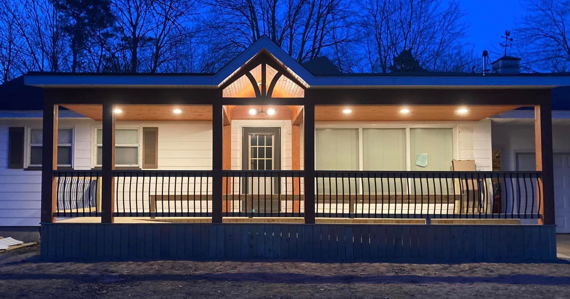 Front view of a lit modern house porch at dusk with wooden railings and blue evening sky