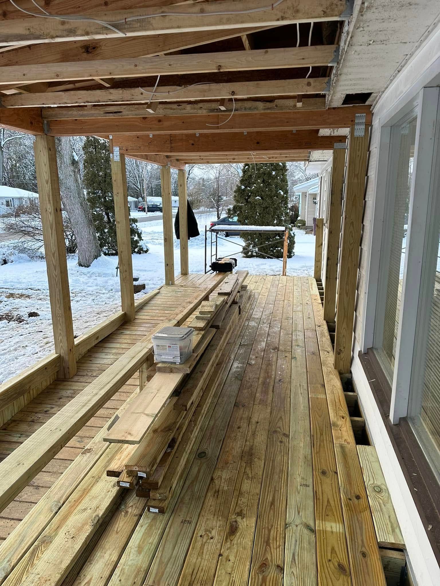 Partially built wooden porch with exposed joists and snow-covered yard beyond
