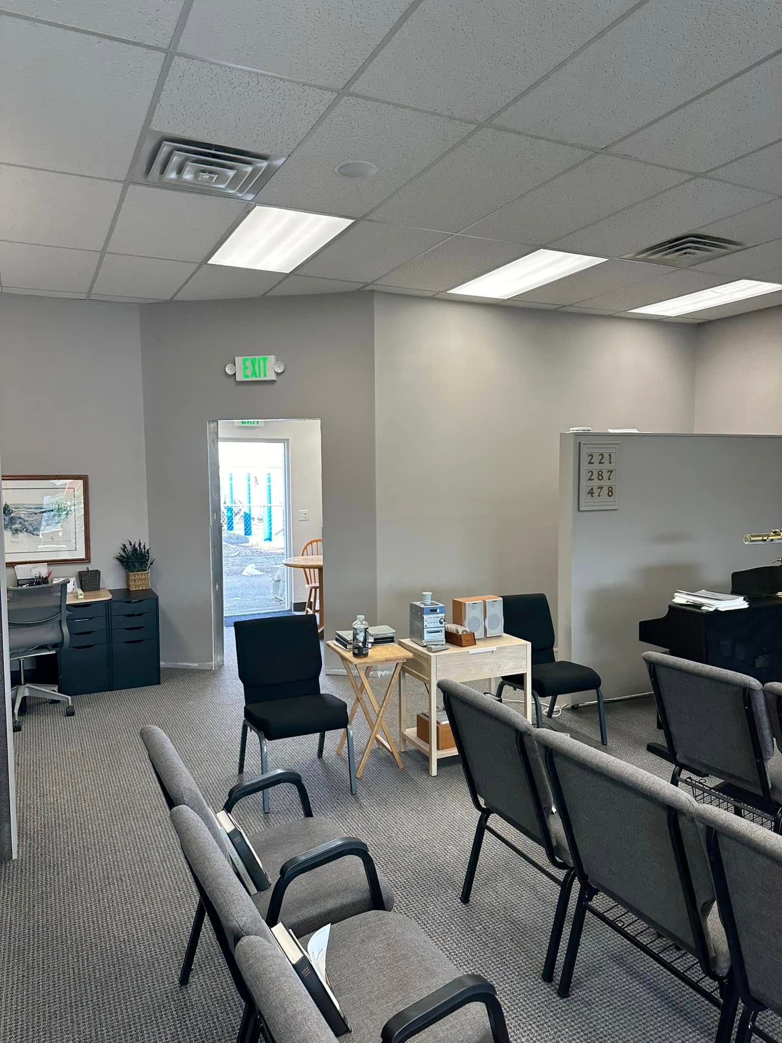 Office lounge with chairs, tables, and a doorway under bright ceiling lights