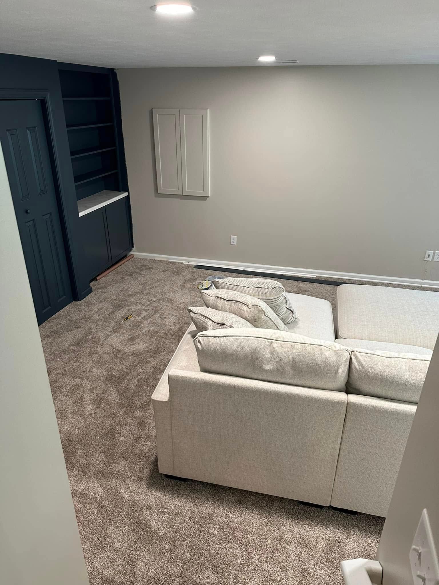 Empty carpeted basement living room with gray walls and a beige sectional sofa