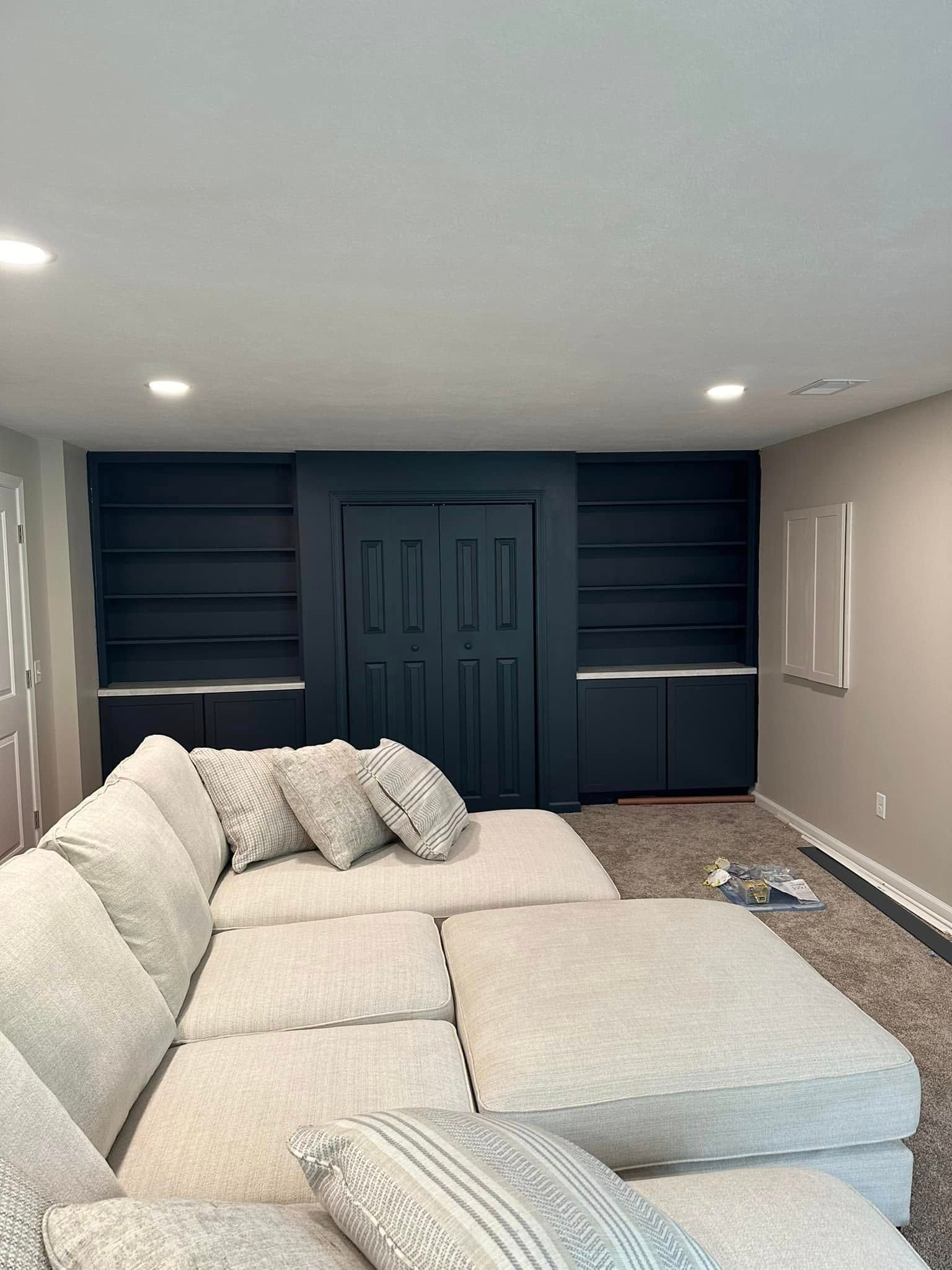 Modern living room with a large white sectional sofa and built-in dark blue shelving behind a central door.