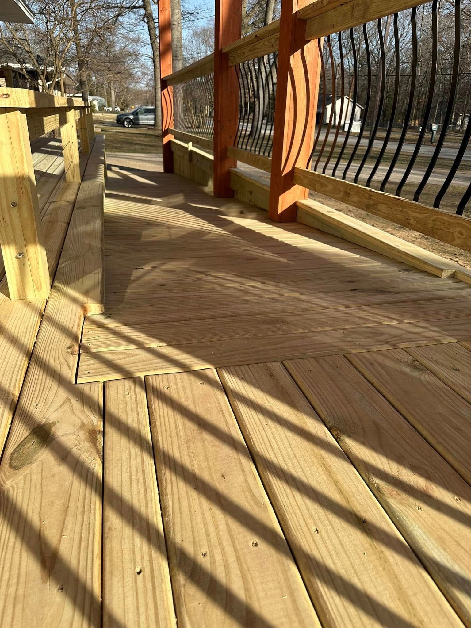 Wooden boardwalk in sunlight beside a black metal fence and orange posts.