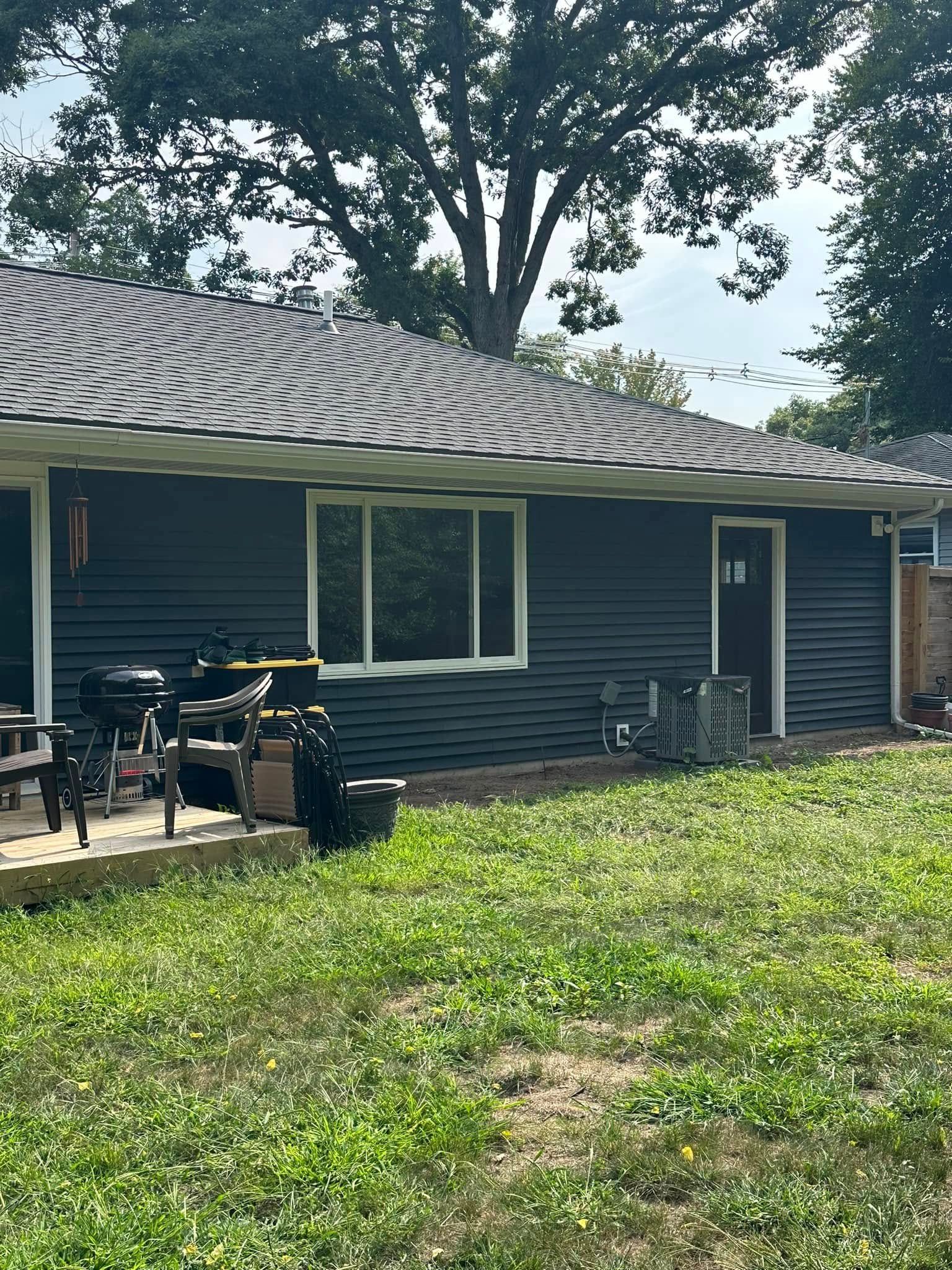 Dark blue house with patio furniture and a large tree in a grassy yard