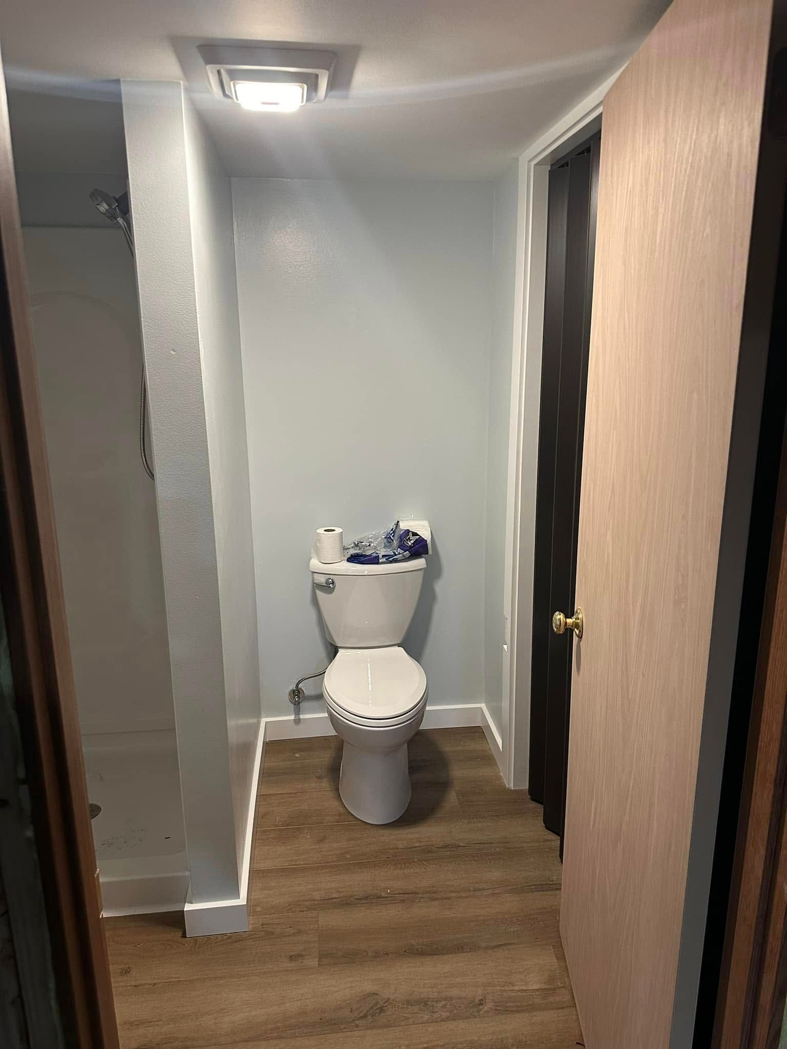 Narrow bathroom with white toilet, wood floor, and gray walls, viewed from the doorway