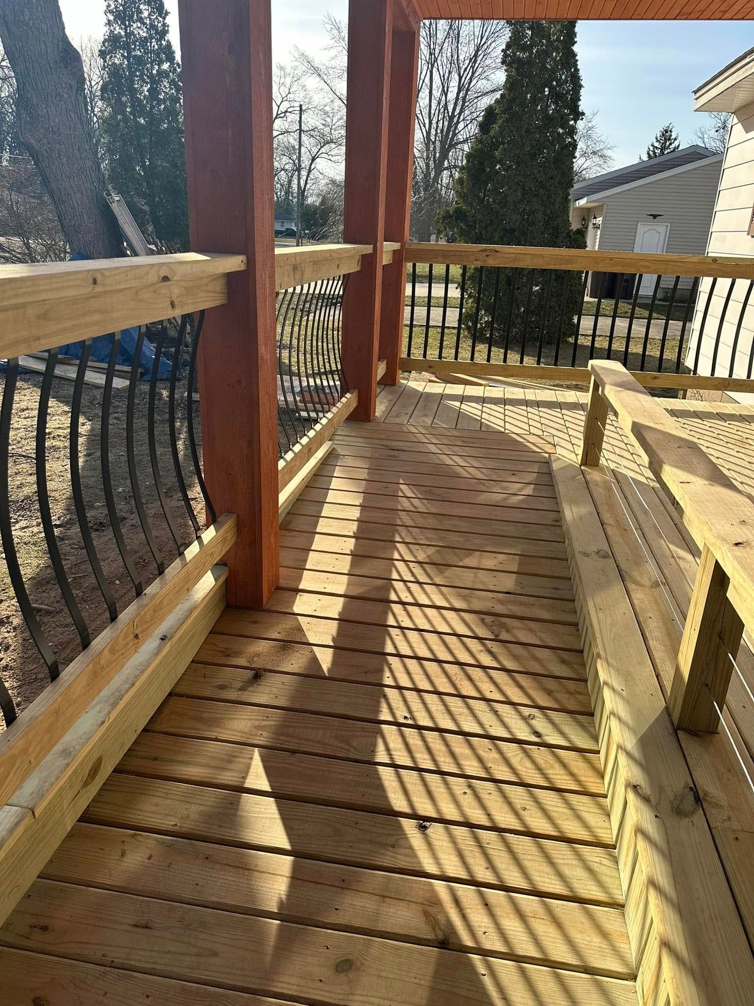 Wooden deck with curved black railing, sunlit floorboards, and trees overlooking a yard