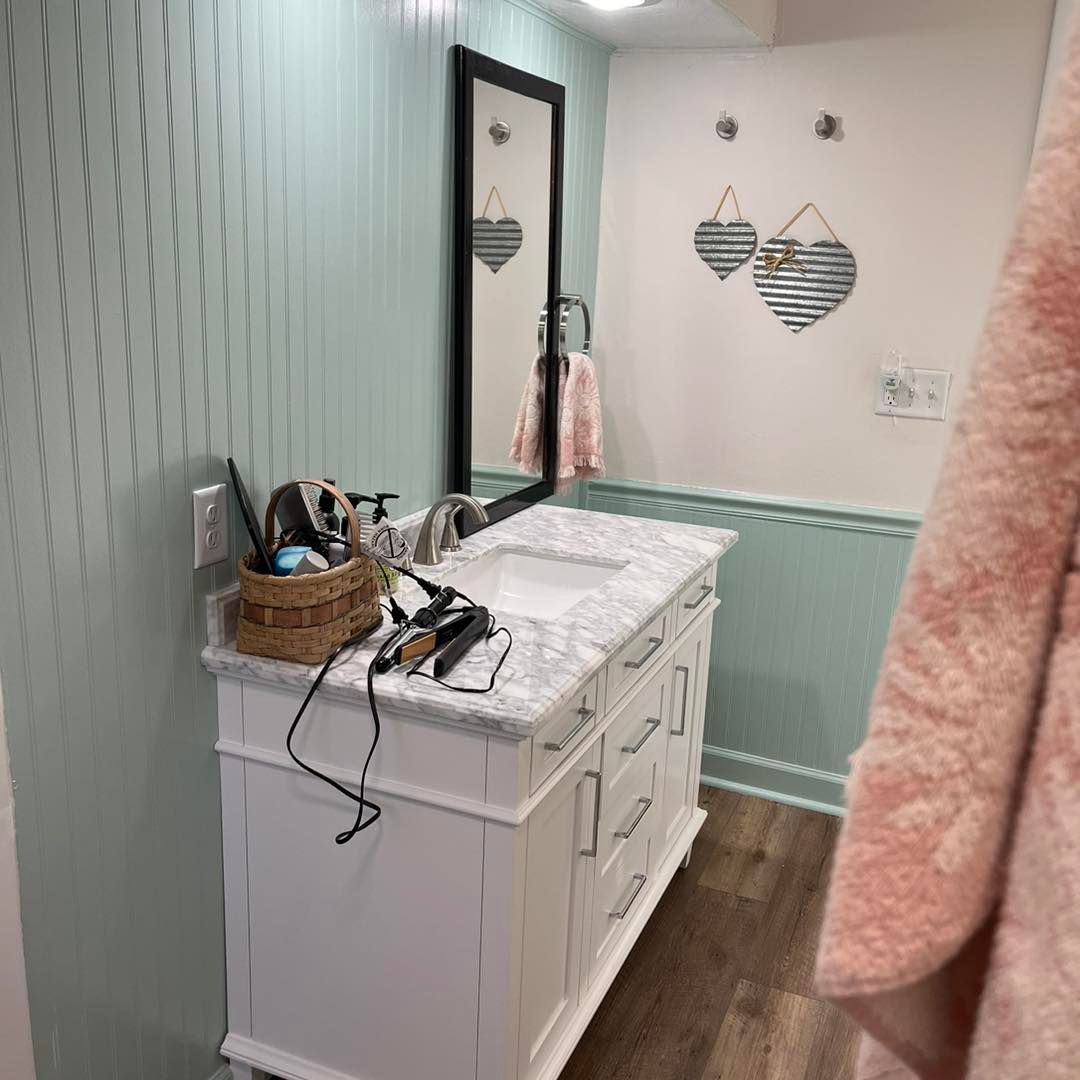 Bright bathroom vanity with marble countertop, mirror, striped wall decor, and a pink towel hanging on the right.
