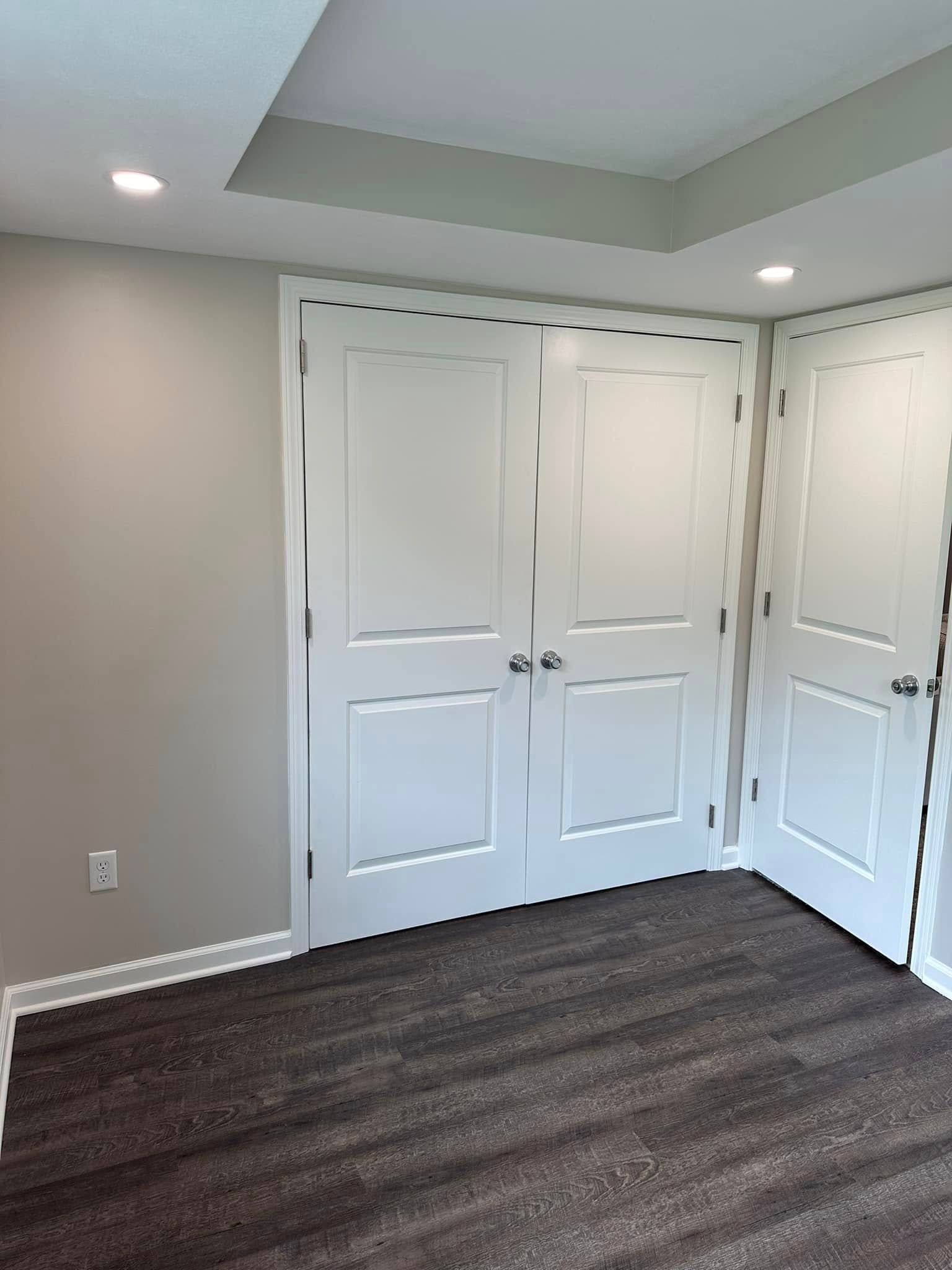 Empty beige room with white double closet doors and dark carpet flooring