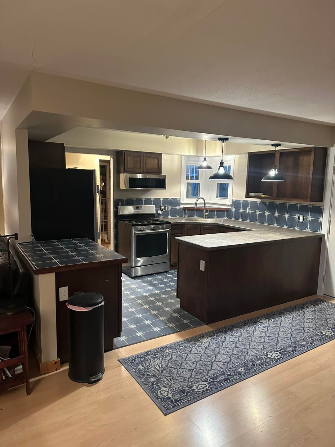 Open kitchen and living area with dark cabinets, island, patterned backsplash, and rug on wood floor