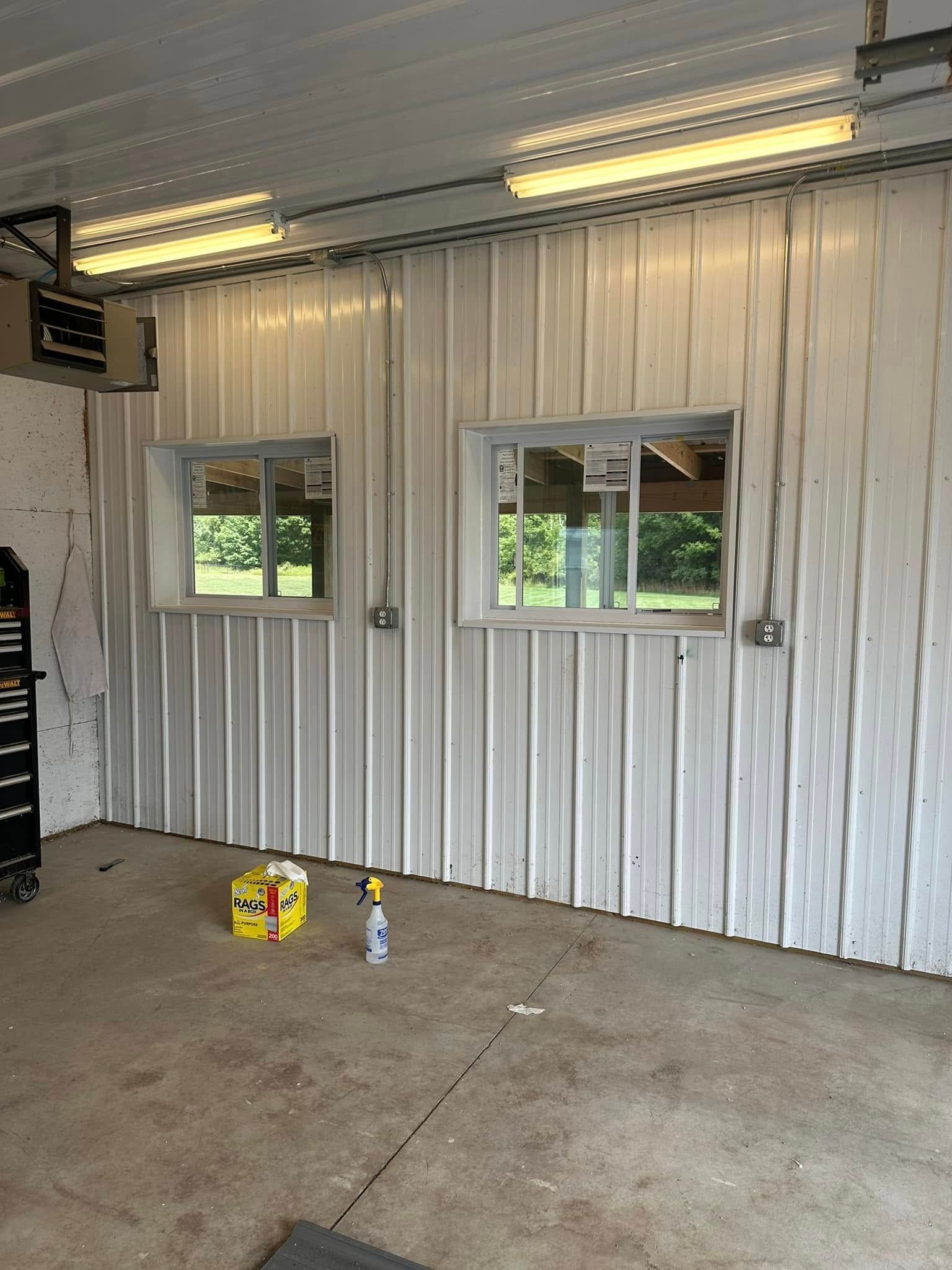 Empty garage with corrugated metal walls, two windows, and fluorescent ceiling lights.