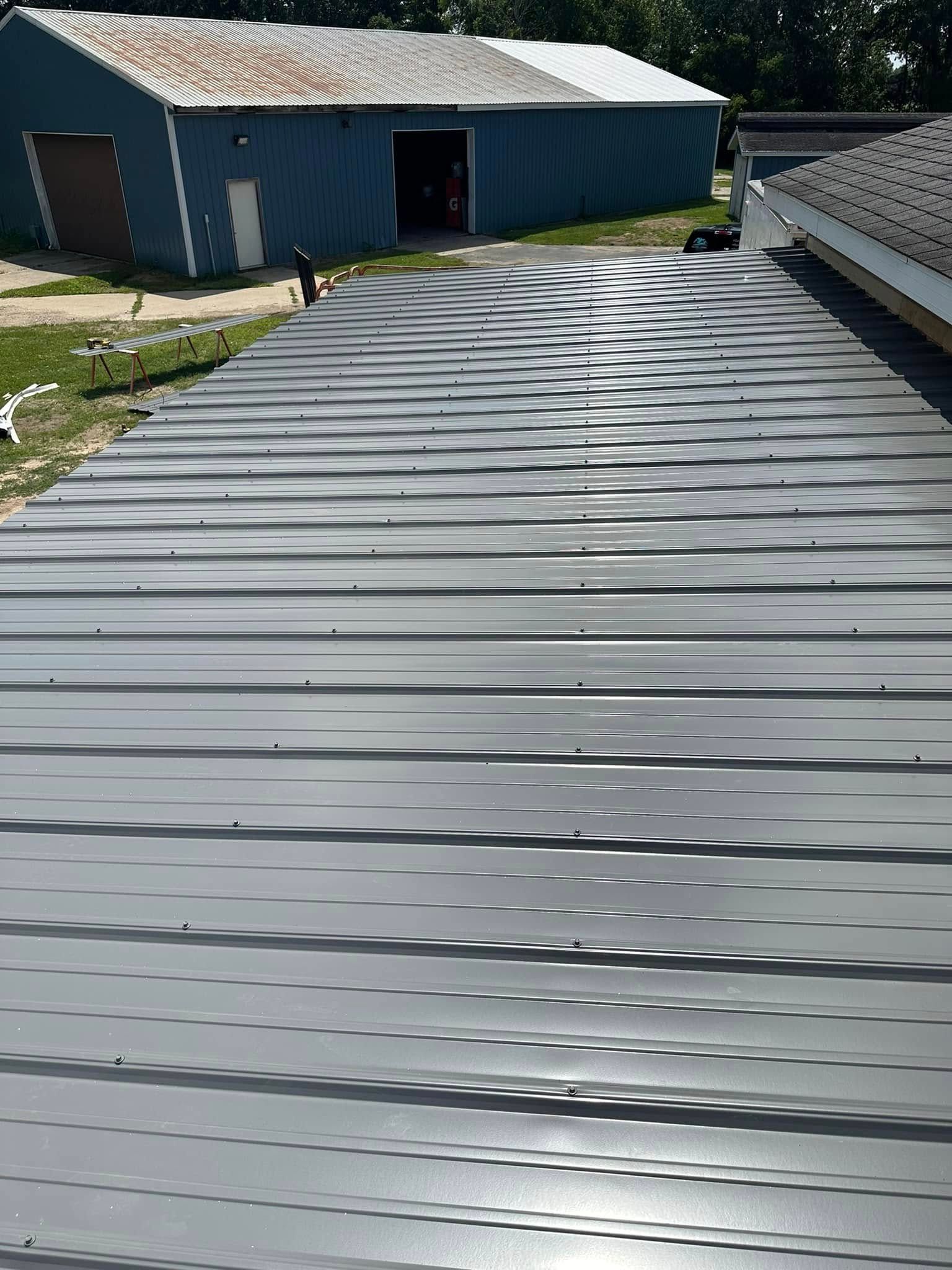 Rooftop with corrugated metal panels leading toward blue farm buildings on a sunny day