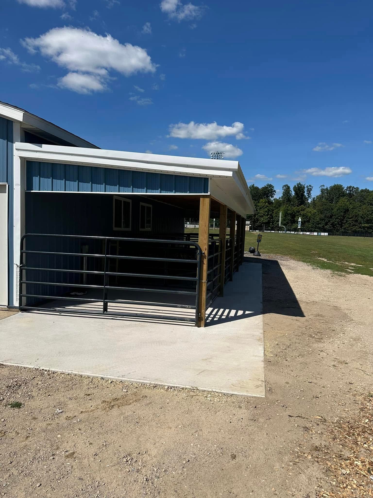 Small black shed with white roof on a concrete pad under a blue sky, surrounded by dirt and open field