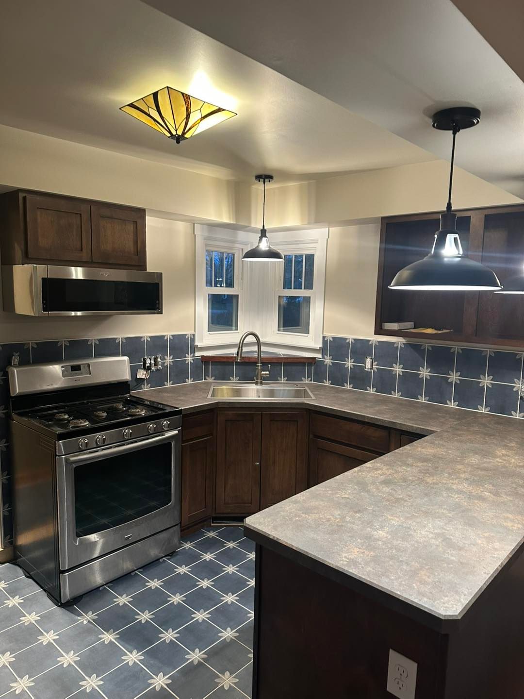 Small kitchen with dark cabinets, gray counters, blue tile backsplash, and a bay window sink.