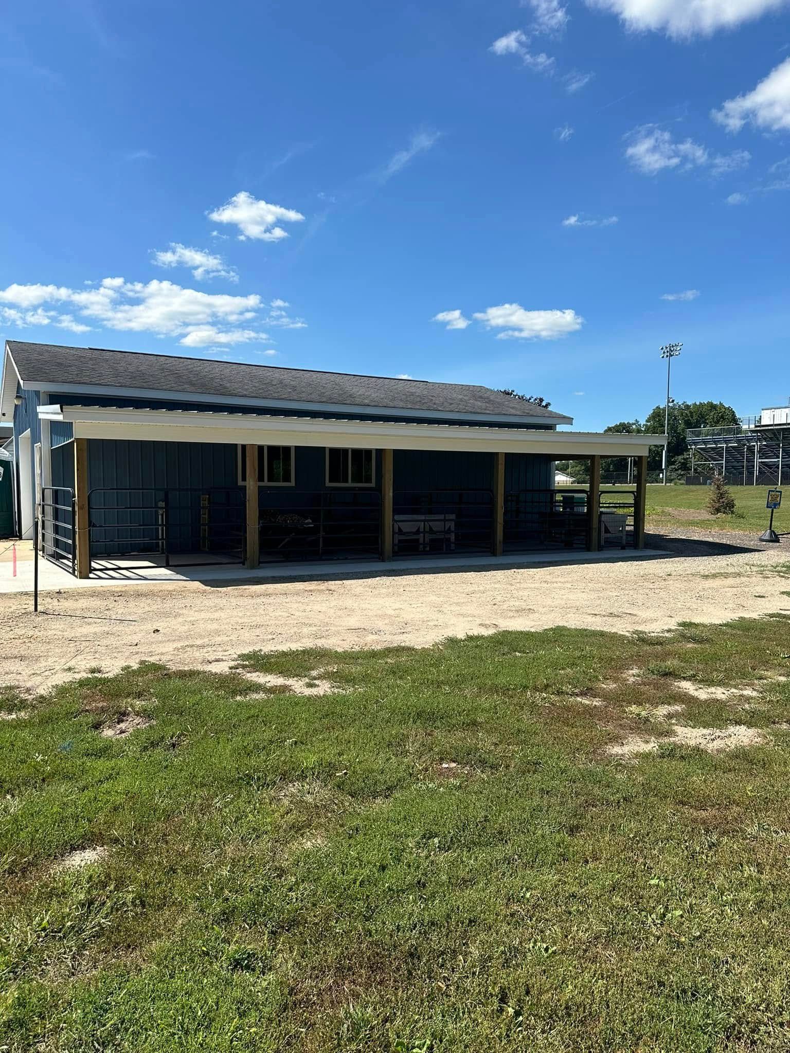 Small open-sided shed with solar panels in a grassy field under a bright blue sky.