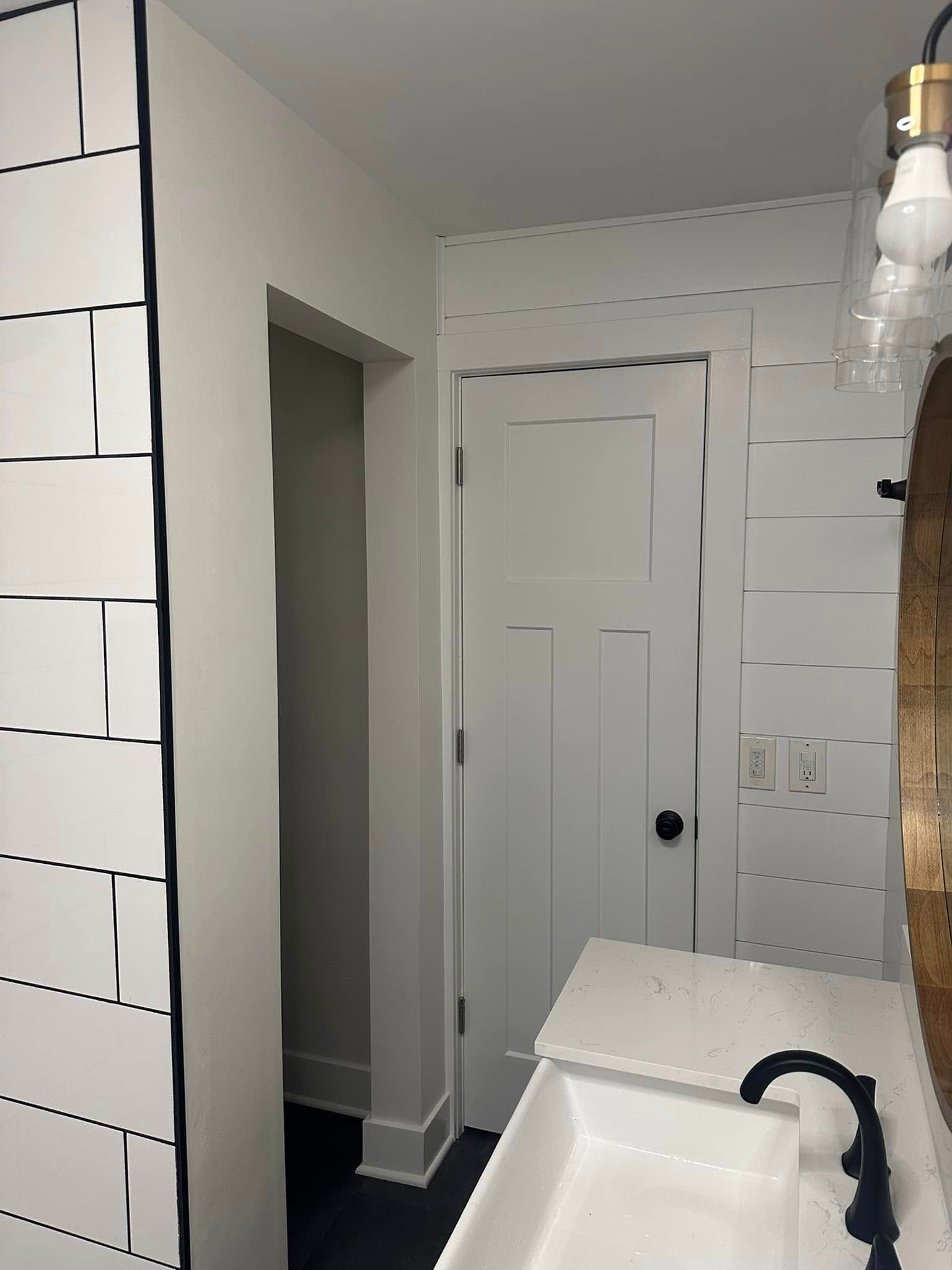 White tiled bathroom with a sink, mirror, and closed paneled door.