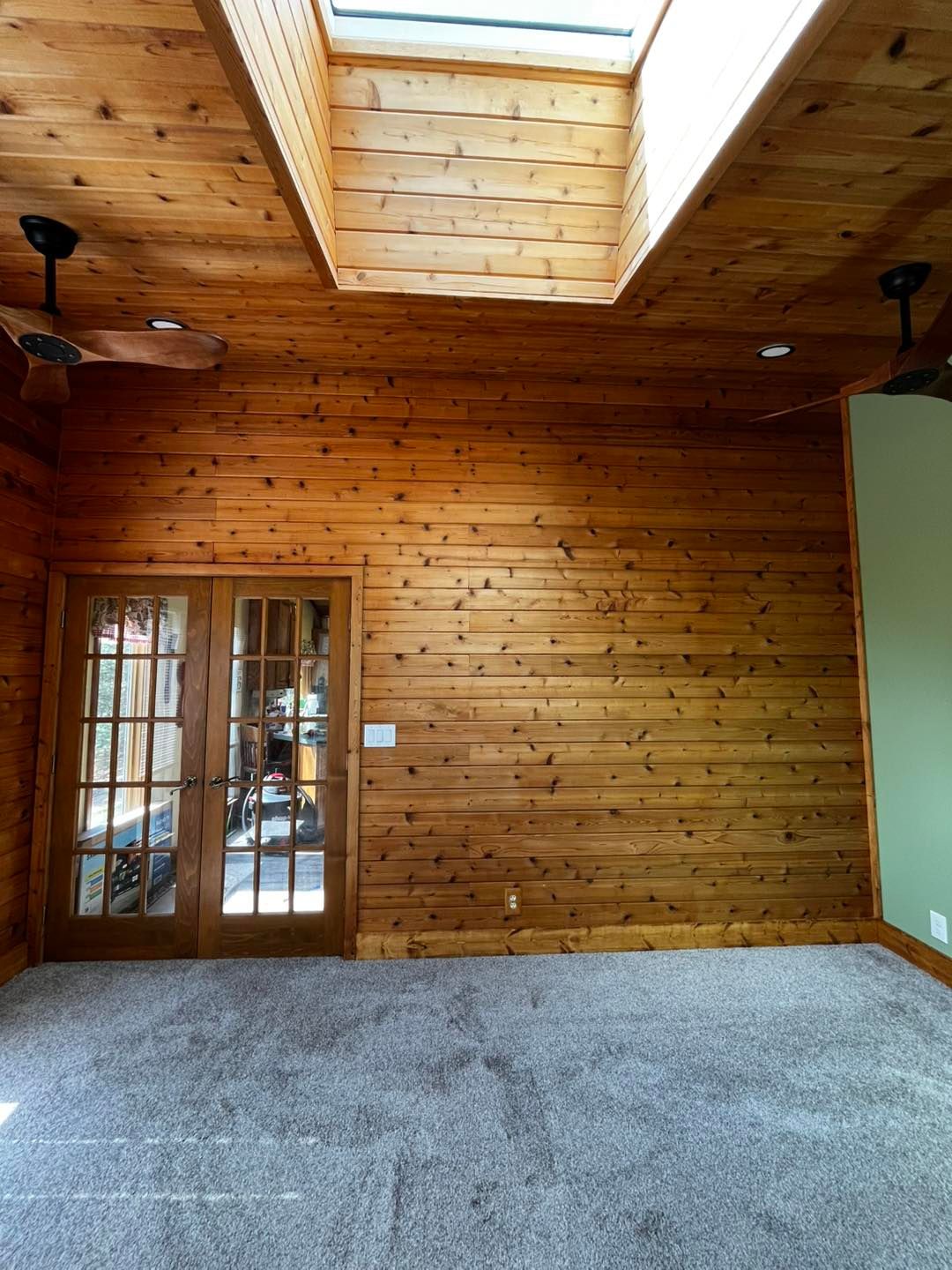 Wood-paneled room with skylight, ceiling fans, French doors, and gray carpet