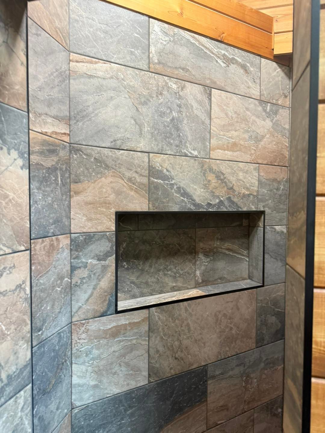 Stone wall with a recessed rectangular fireplace opening in a tiled interior.