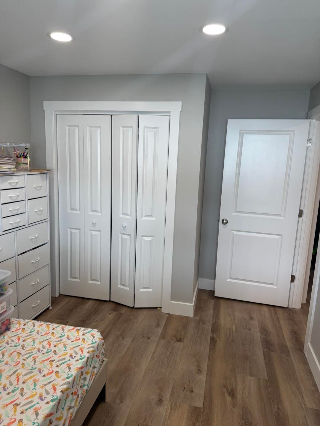 Small bedroom with white closet doors, a white door, dresser, and wood floor under recessed lights