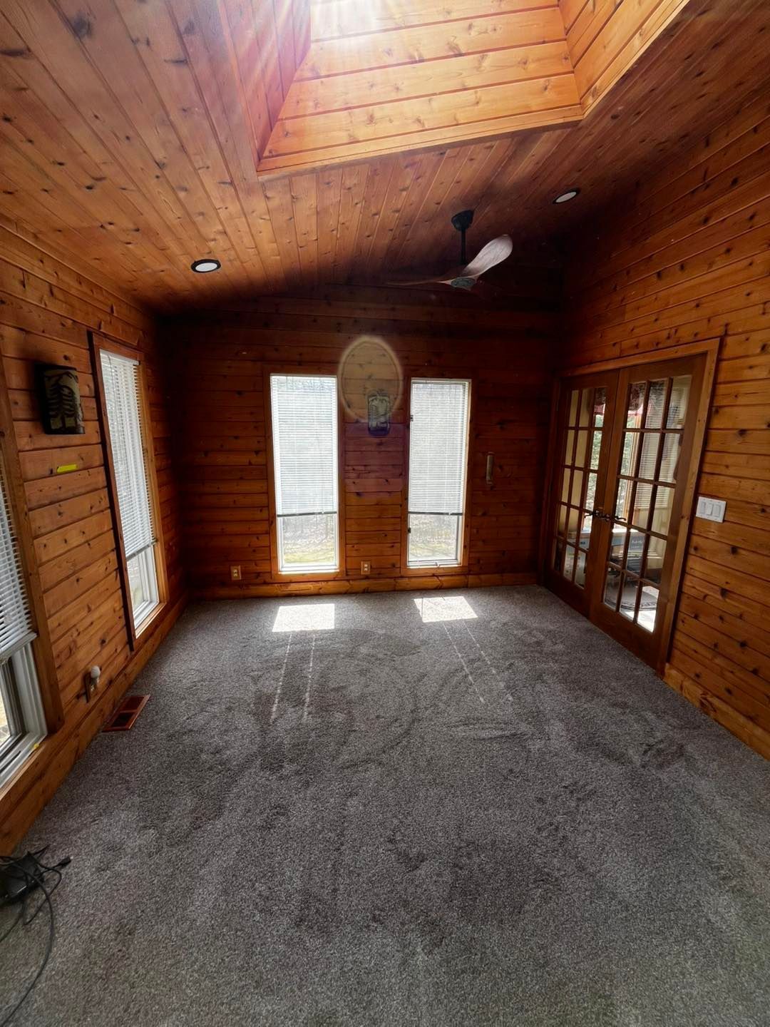 Wood-paneled room with carpet, vaulted ceiling, and French doors opening to a small porch.