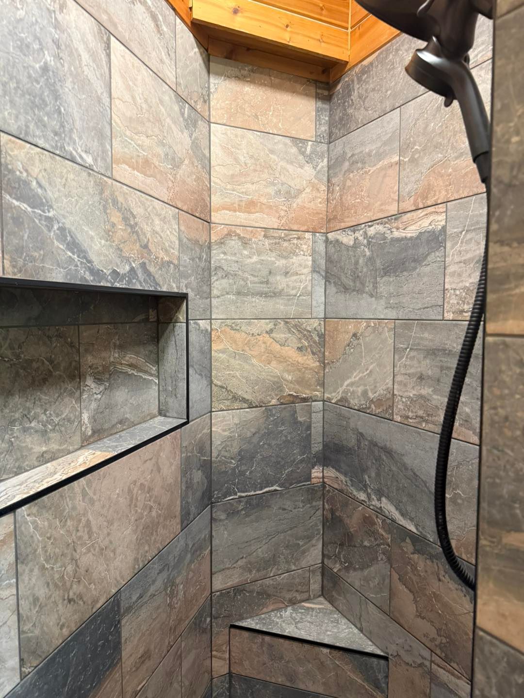 Stone-tiled shower with built-in bench, recessed shelf, and black handheld showerhead