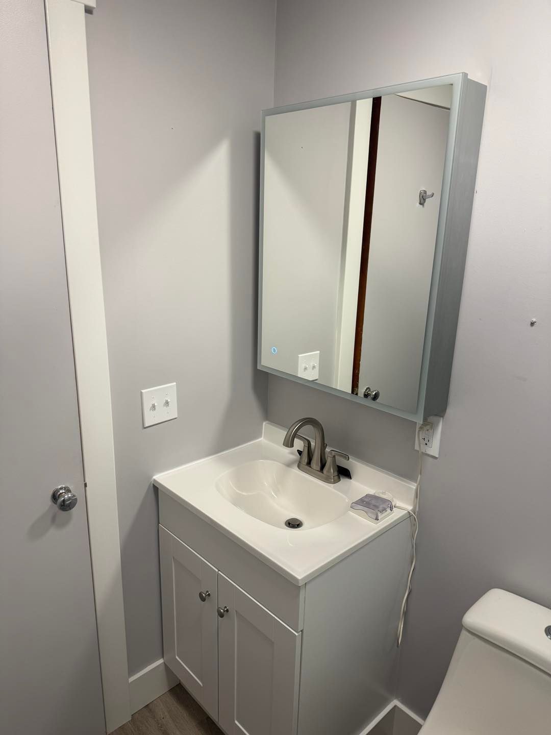 Small bathroom vanity with mirror, white cabinet, sink, and gray walls.