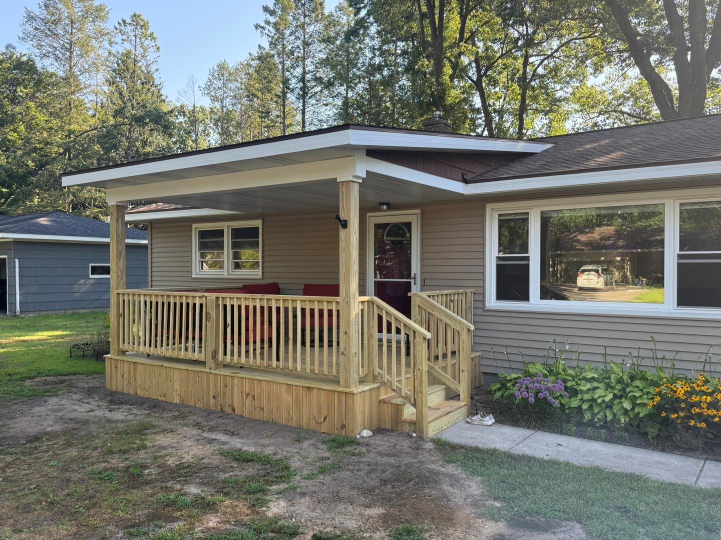 Small beige house with a covered front porch, wooden ramp, and yellow flowers in the yard