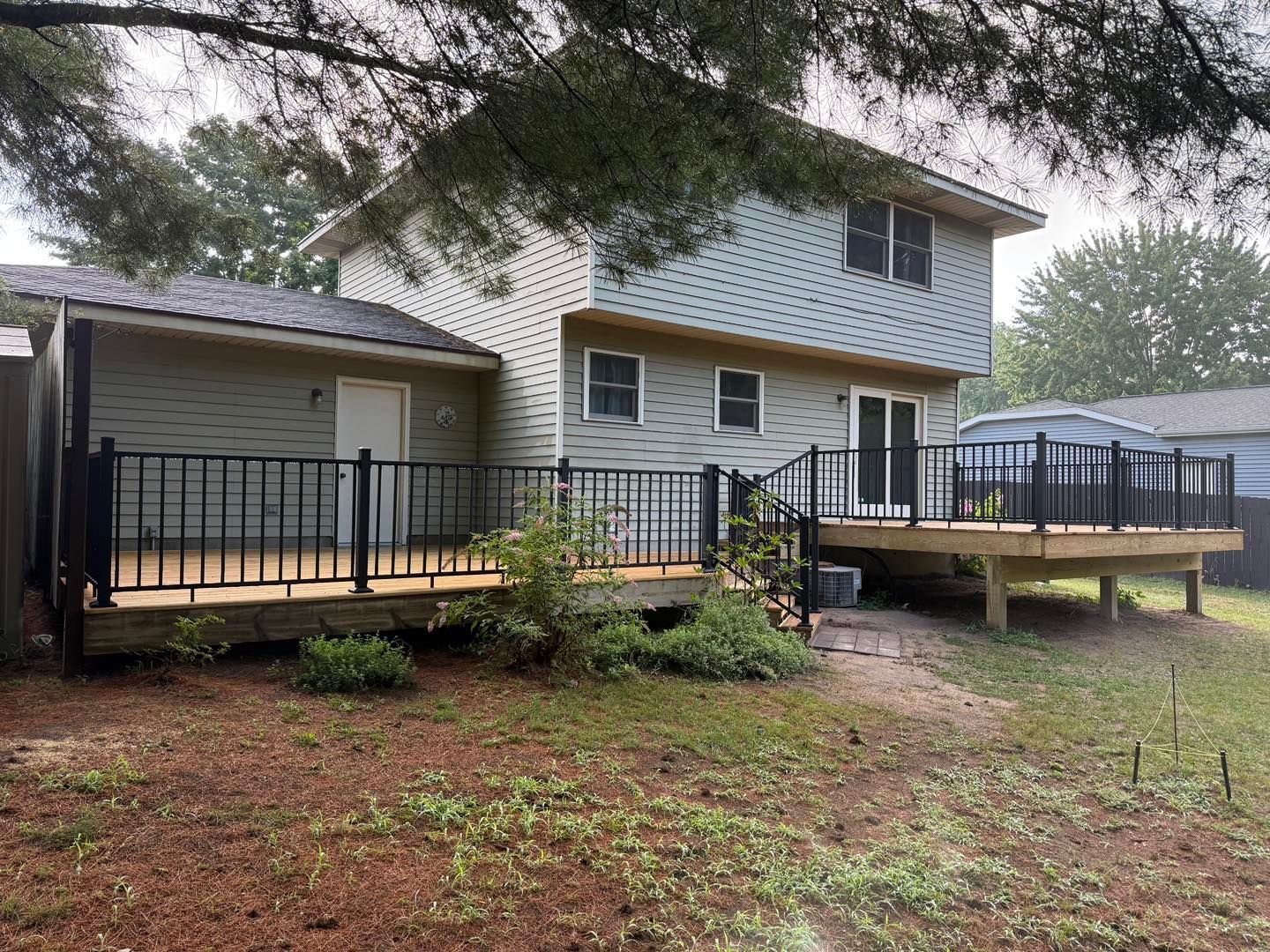 Two-story house with a wooden deck and black railings in a wooded yard on a cloudy day