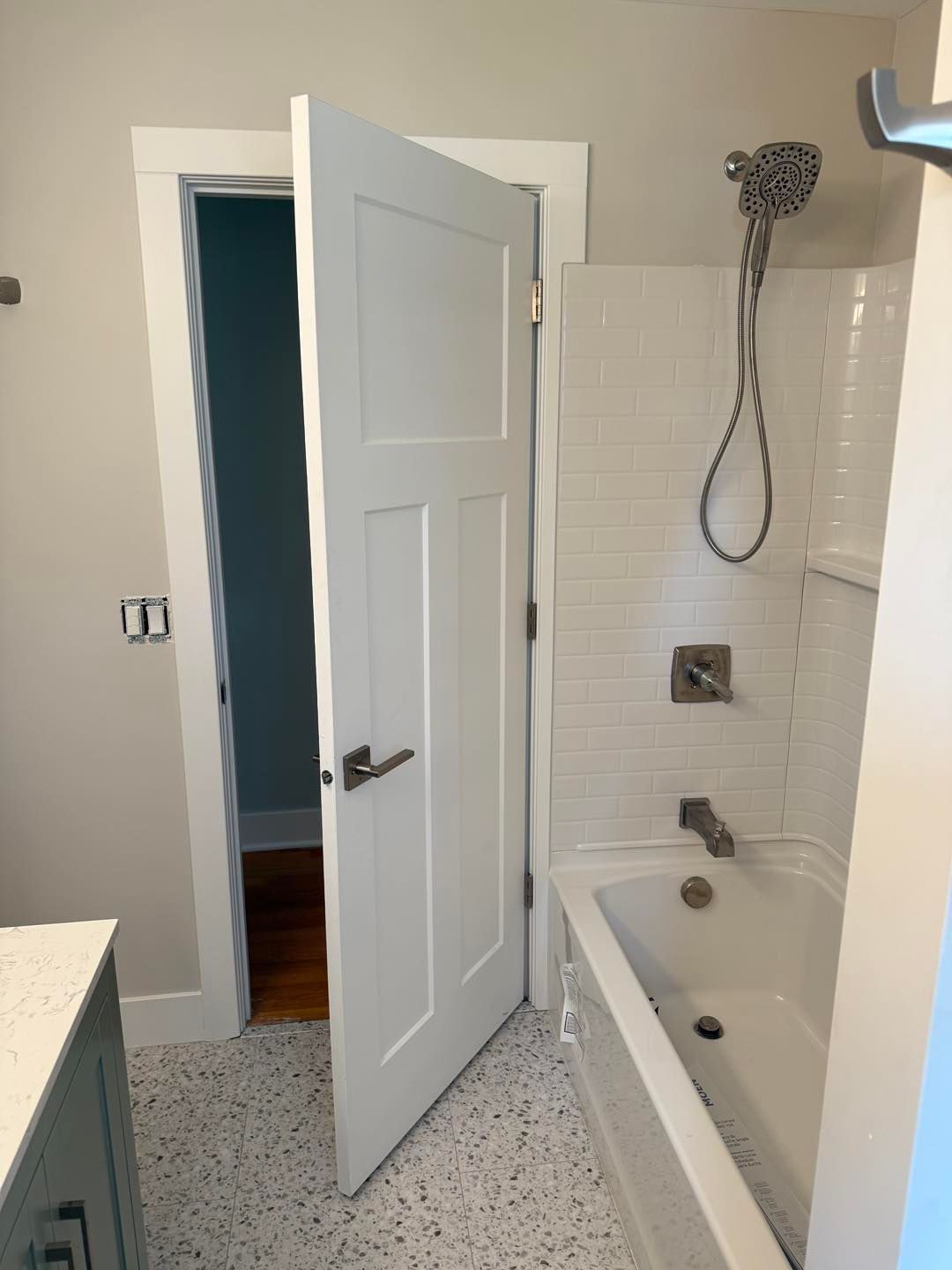 Bathroom with white tub-shower, tiled surround, and open door to a hallway.